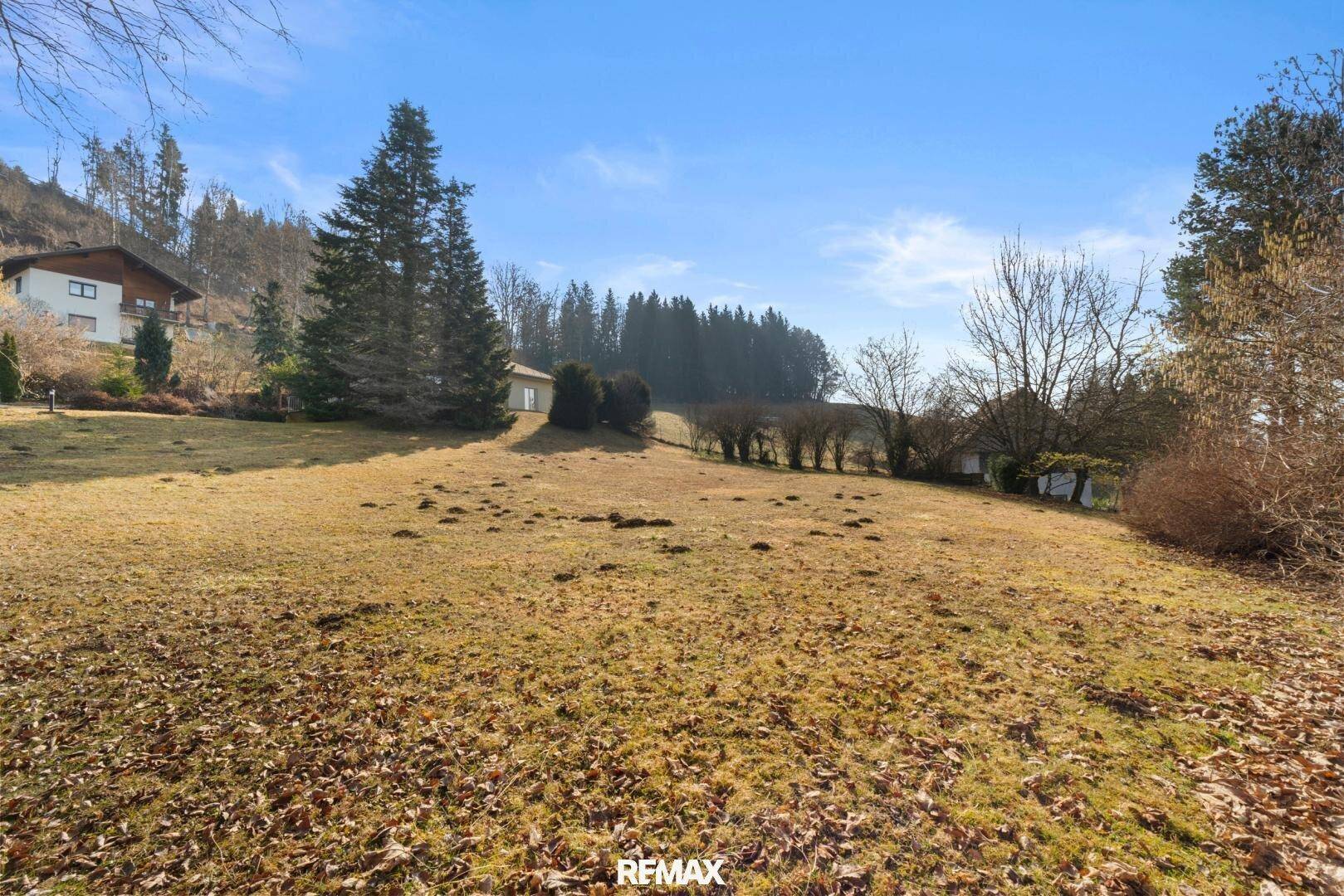 Große Rasenfläche mit Bäumen und Blick auf die umliegende Hügellandschaft und weitere Häuser.