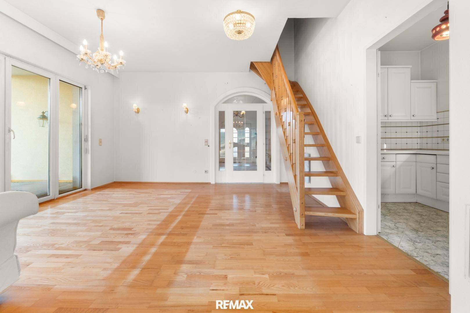 Geräumiges Wohnzimmer mit Holztreppe, Parkettboden und Zugang zu weiteren hellen Räumen.