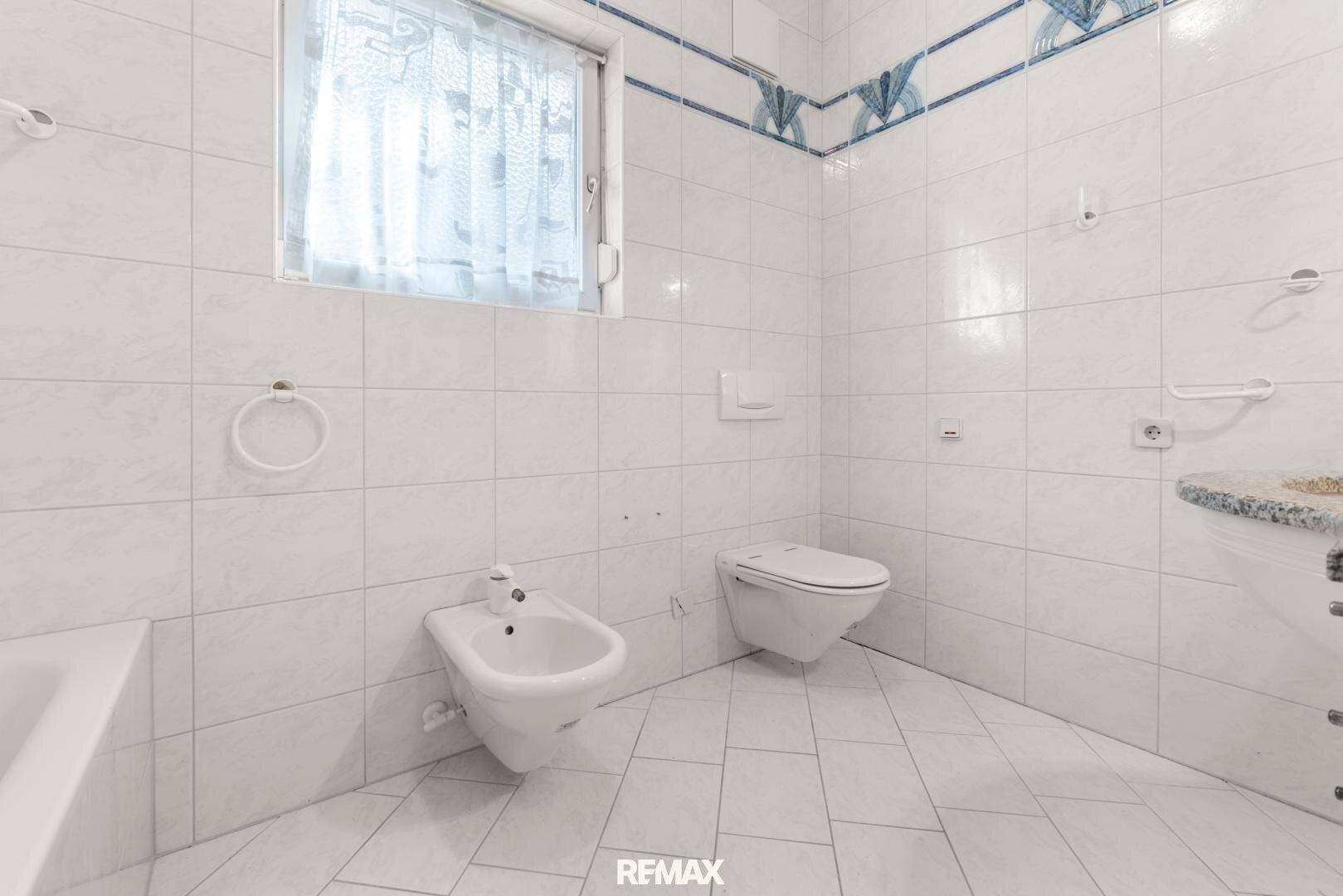 Helles Badezimmer mit Bidet, WC, Fliesen und Fenster für natürliche Belüftung und Tageslicht.