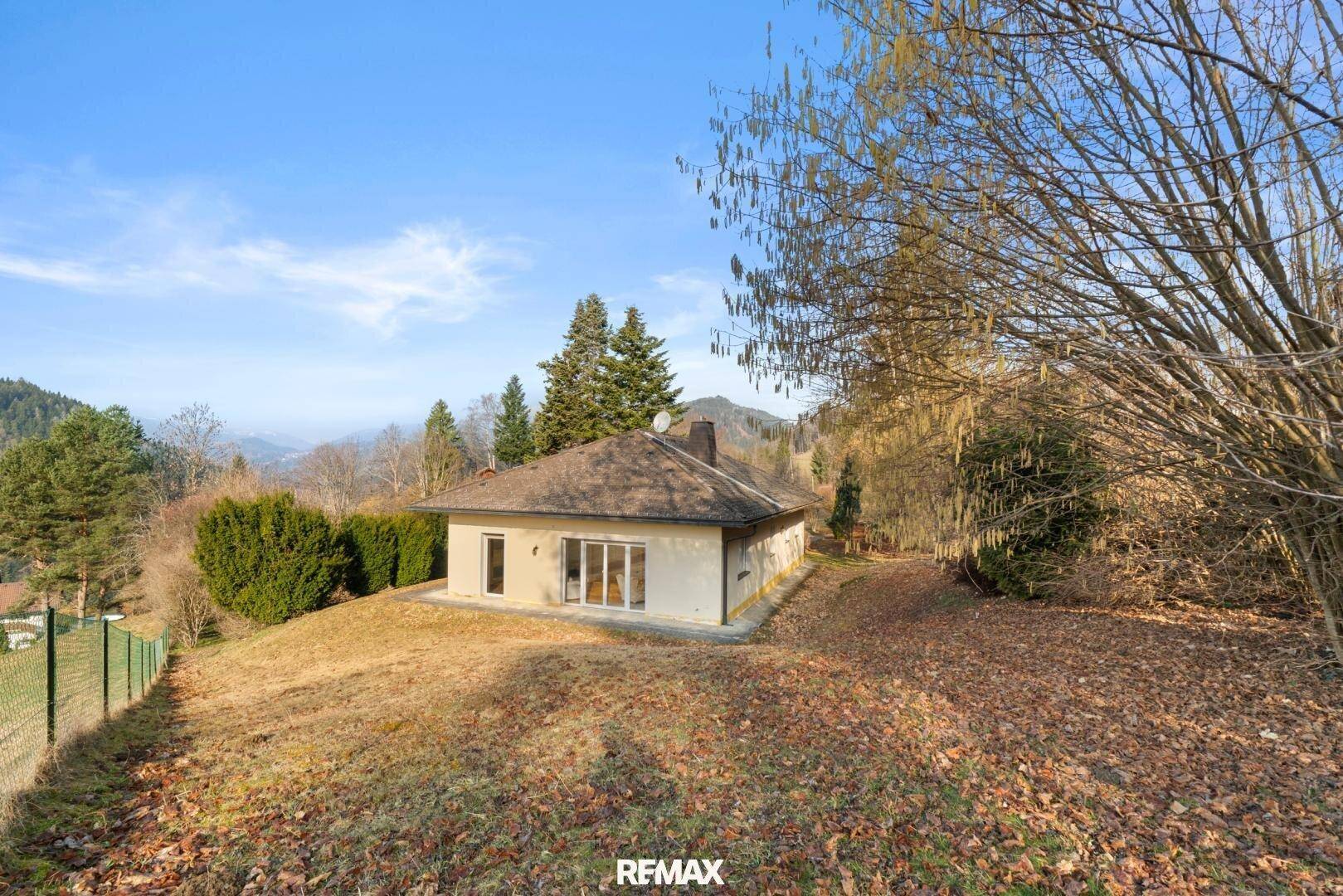 Haus in Hanglage mit weitem Blick über die Landschaft und die umliegende Natur unter blauem Himmel.