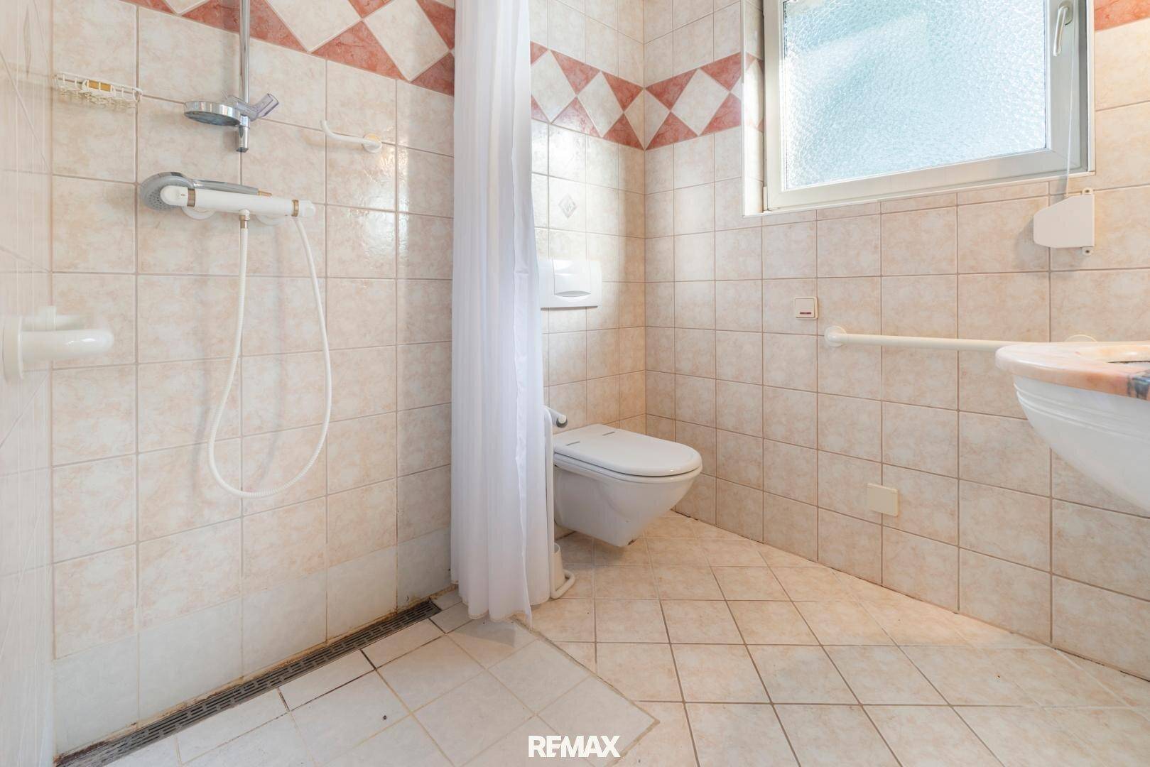 Funktionales Badezimmer mit Dusche, WC, Fliesen und Haltegriffen für mehr Sicherheit und Komfort.