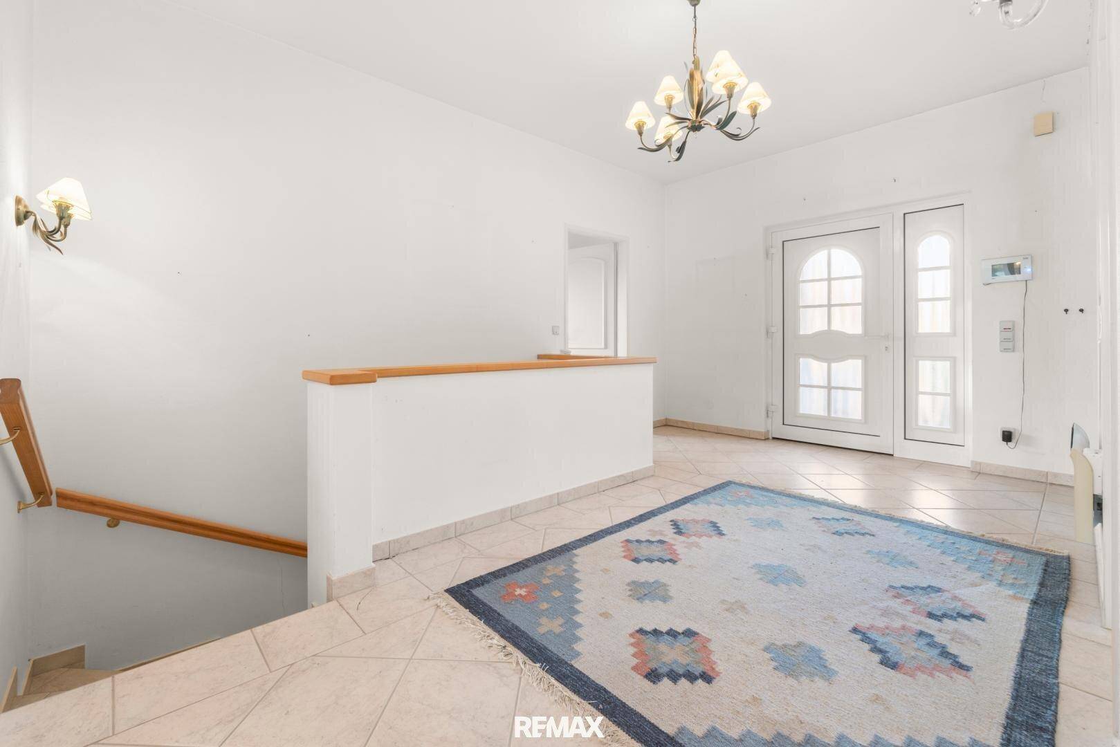 Eingangsbereich mit Fliesenboden, Teppich und einer Holztreppe, die in die obere Etage führt.