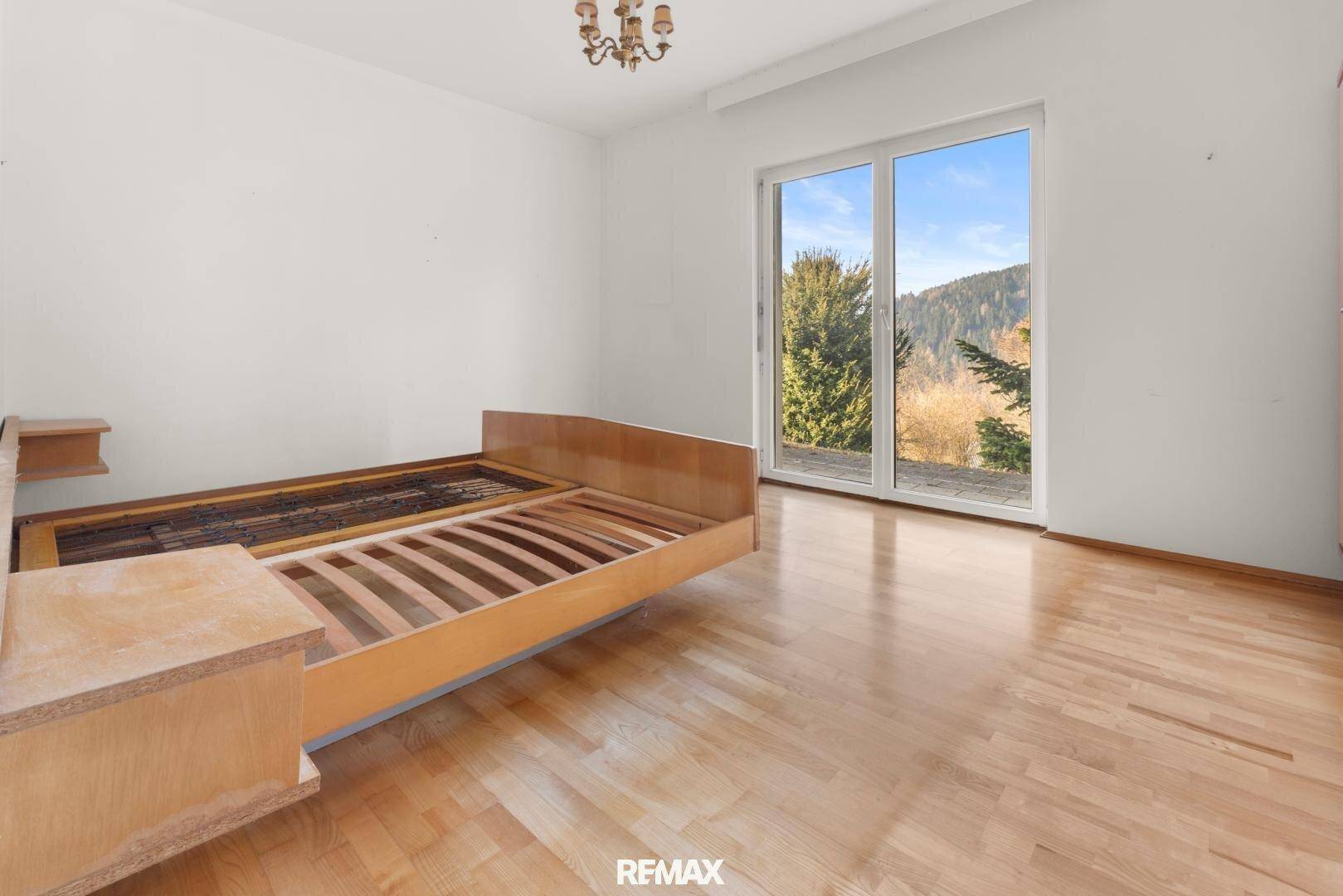 Schlafzimmer mit Parkettboden, Bettrahmen und großen Fenstern mit malerischem Bergblick.