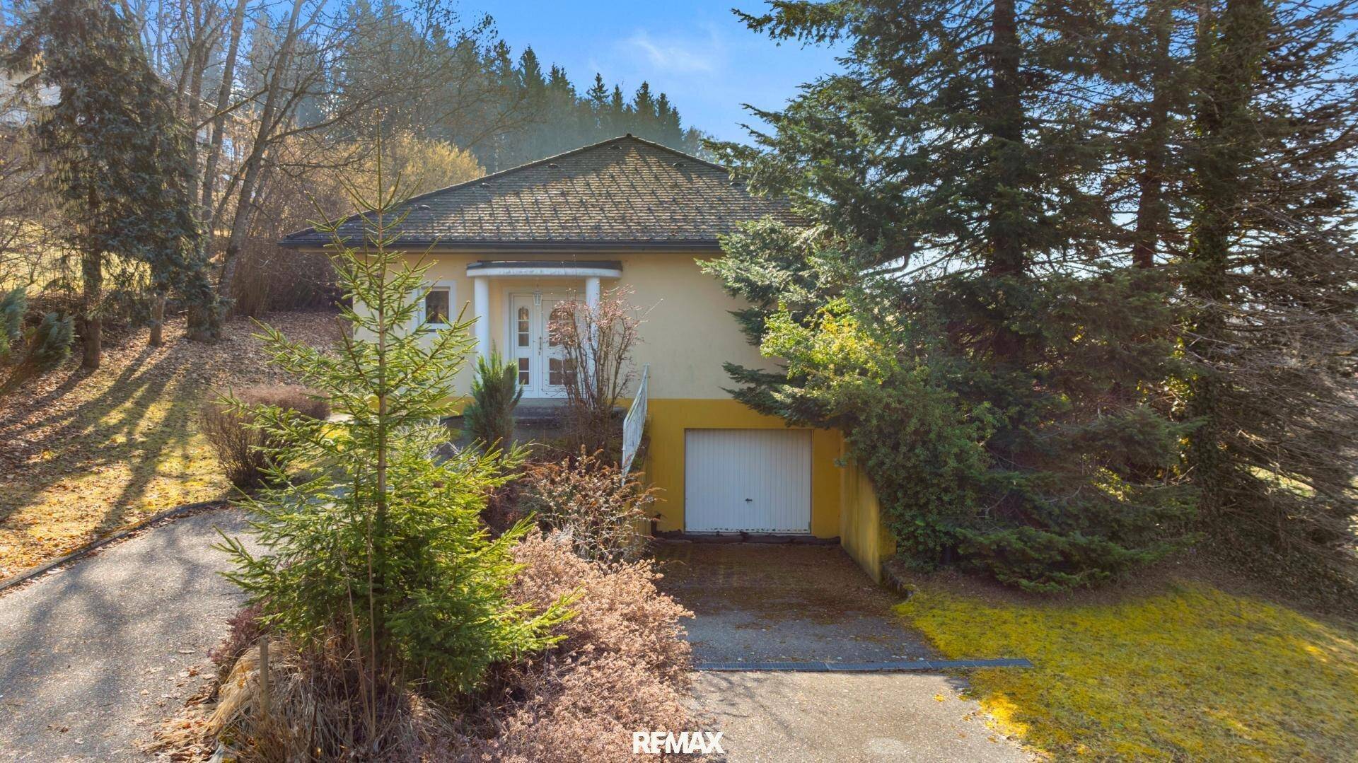 Einfamilienhaus mit integrierter Garage, umgeben von Bäumen und einer gepflasterten Auffahrt.