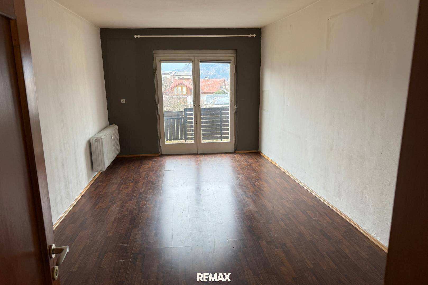 Raum mit Laminatboden und Zugang zu einem Balkon, der viel natürliches Licht bietet.