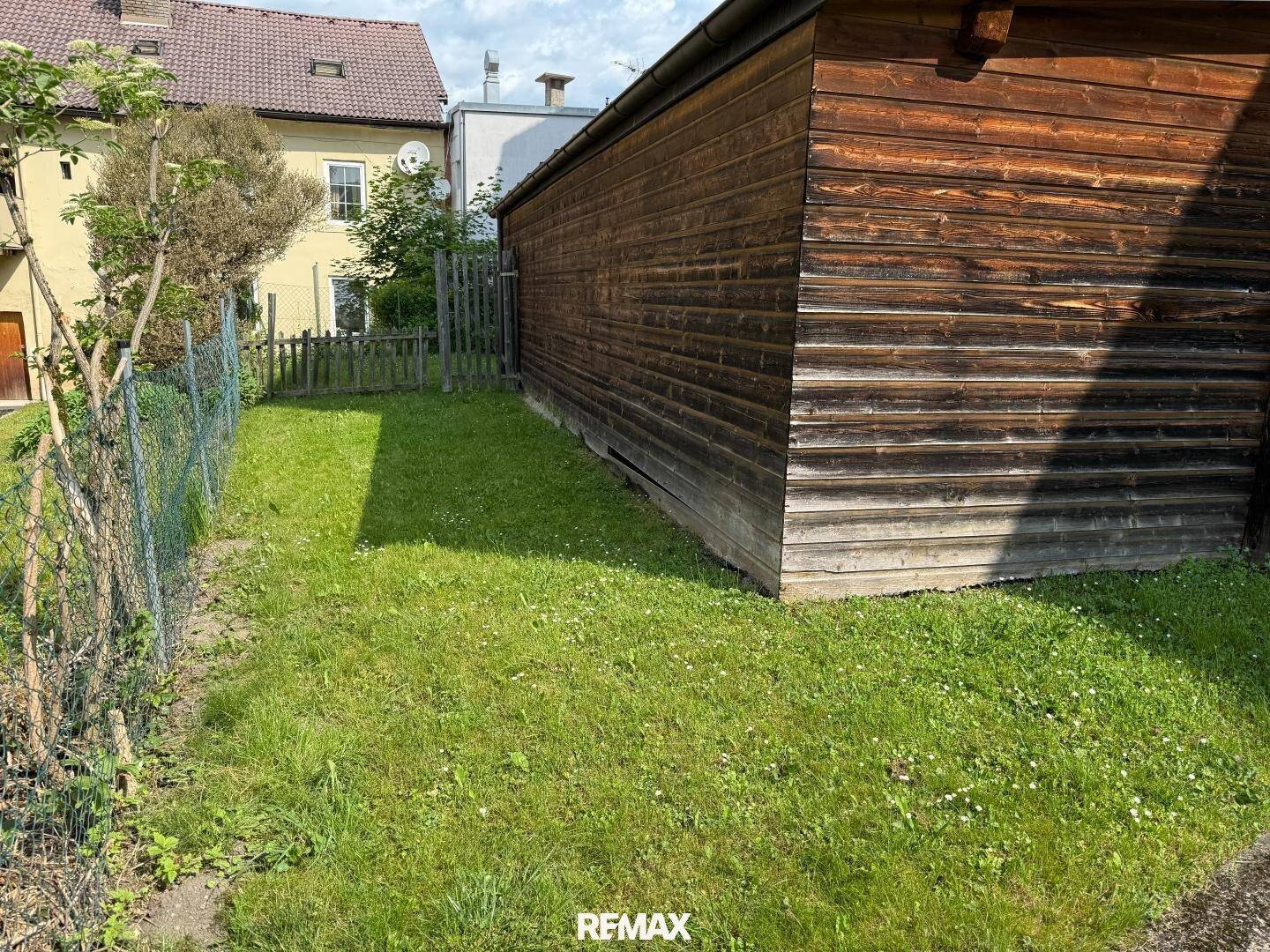 Grüner Gartenbereich mit Rasen und einem Zaun, der an einen Holzschuppen grenzt.