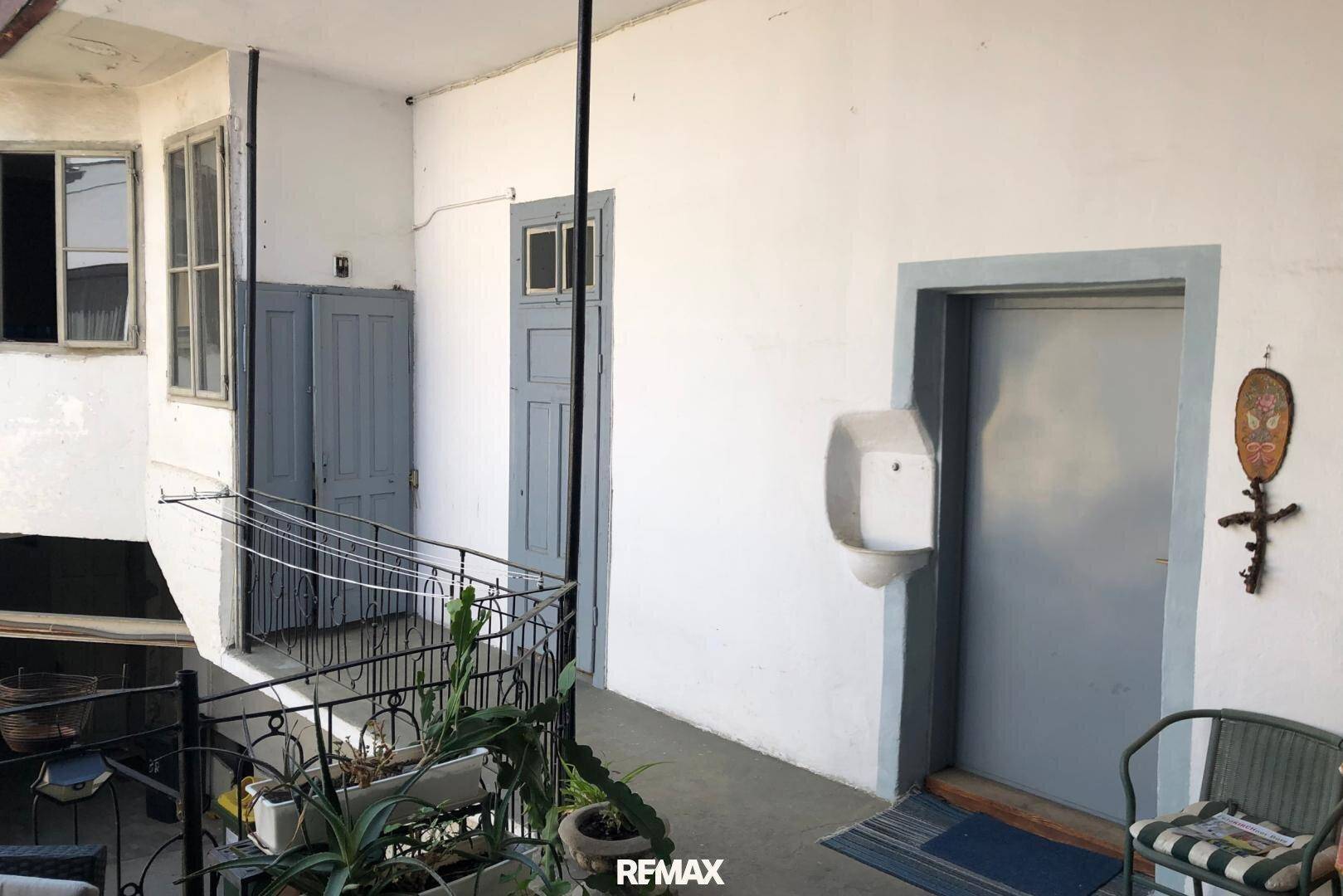 Heller Innenhof mit einem Balkon, Pflanzen und einer Tür, die zu einem Innenbereich führt.