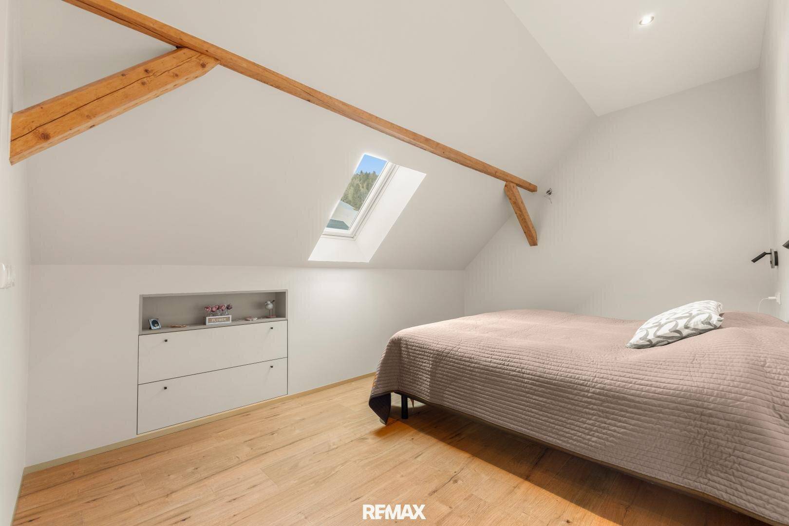 Gemütliches Schlafzimmer im Dachgeschoss mit Holzbalken, Dachfenster und Holzboden.