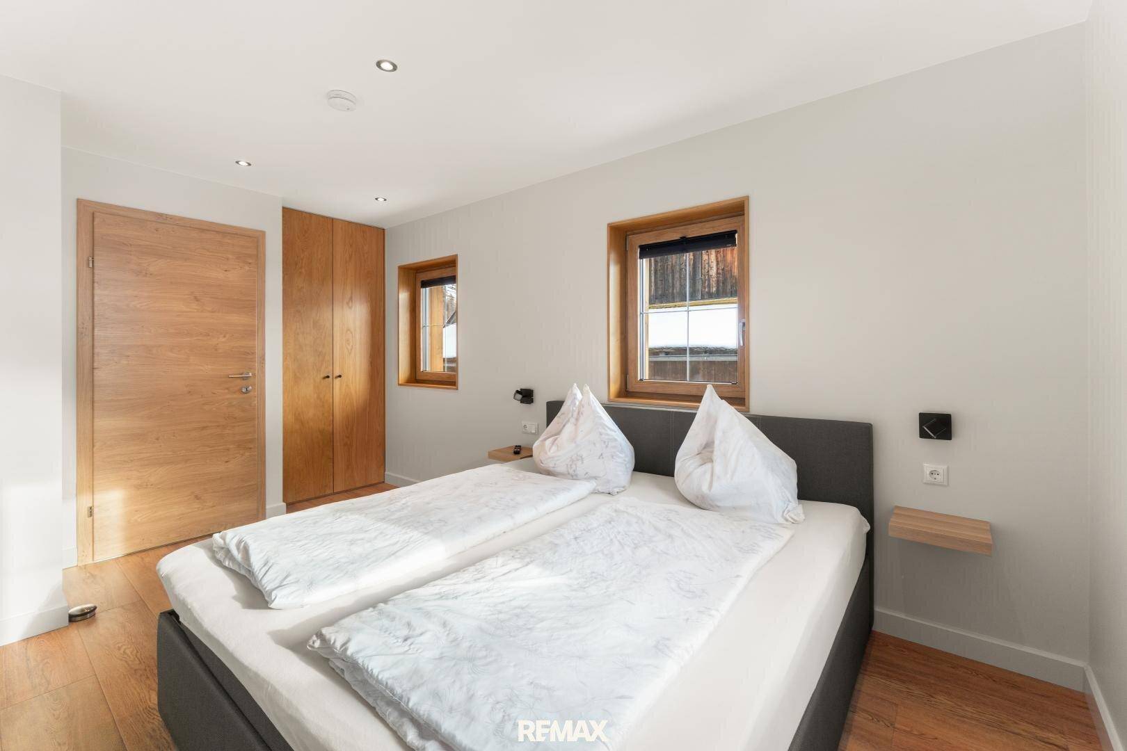 Helles Schlafzimmer mit Holzboden, Einbauschränken und zwei Fenstern.