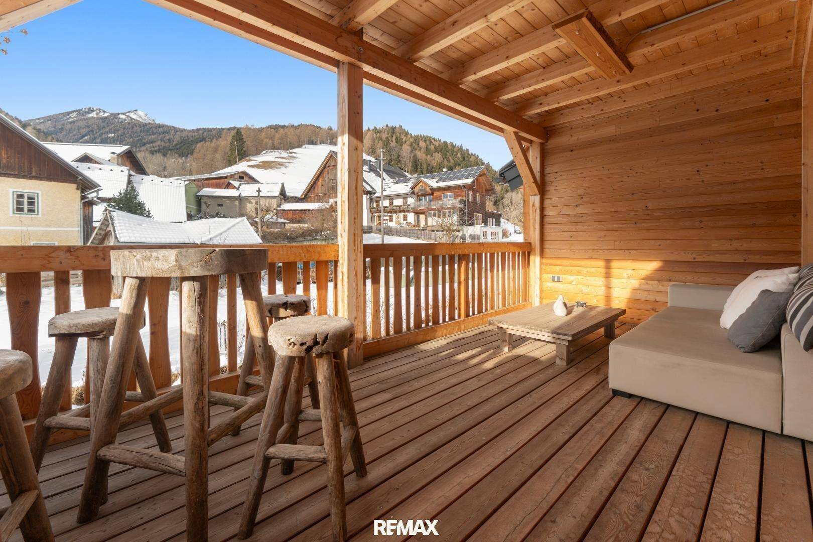 Überdachter Holzbalkon mit Barhockern und Blick auf die verschneite Berglandschaft.
