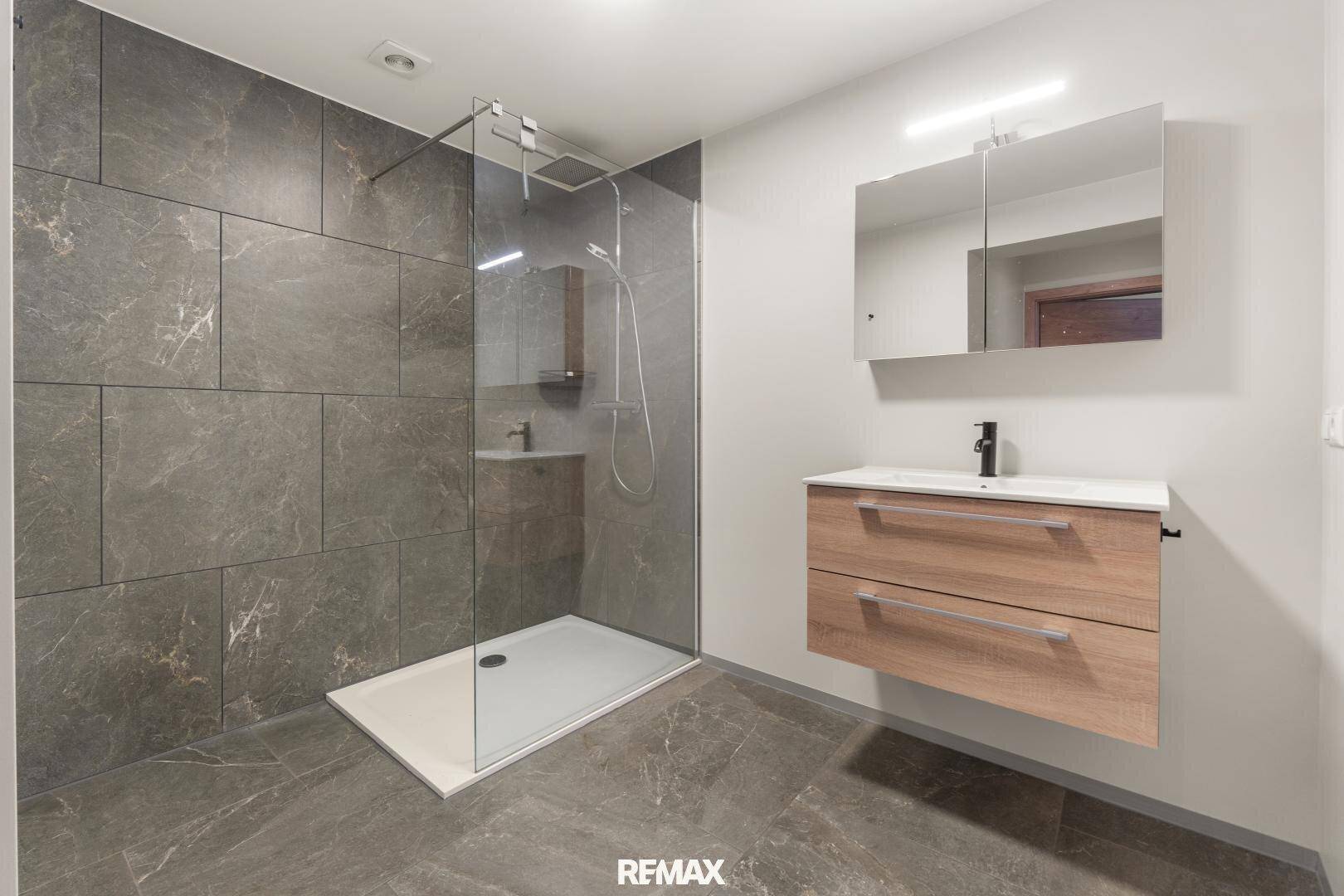 Modernes Badezimmer mit großer begehbarer Dusche, Einzelwaschbecken und Spiegelschrank.