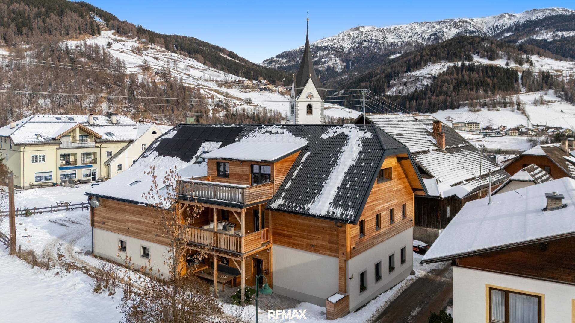Traditionelles Holzhaus mit Balkonen und schneebedecktem Dach in alpiner Berglandschaft.