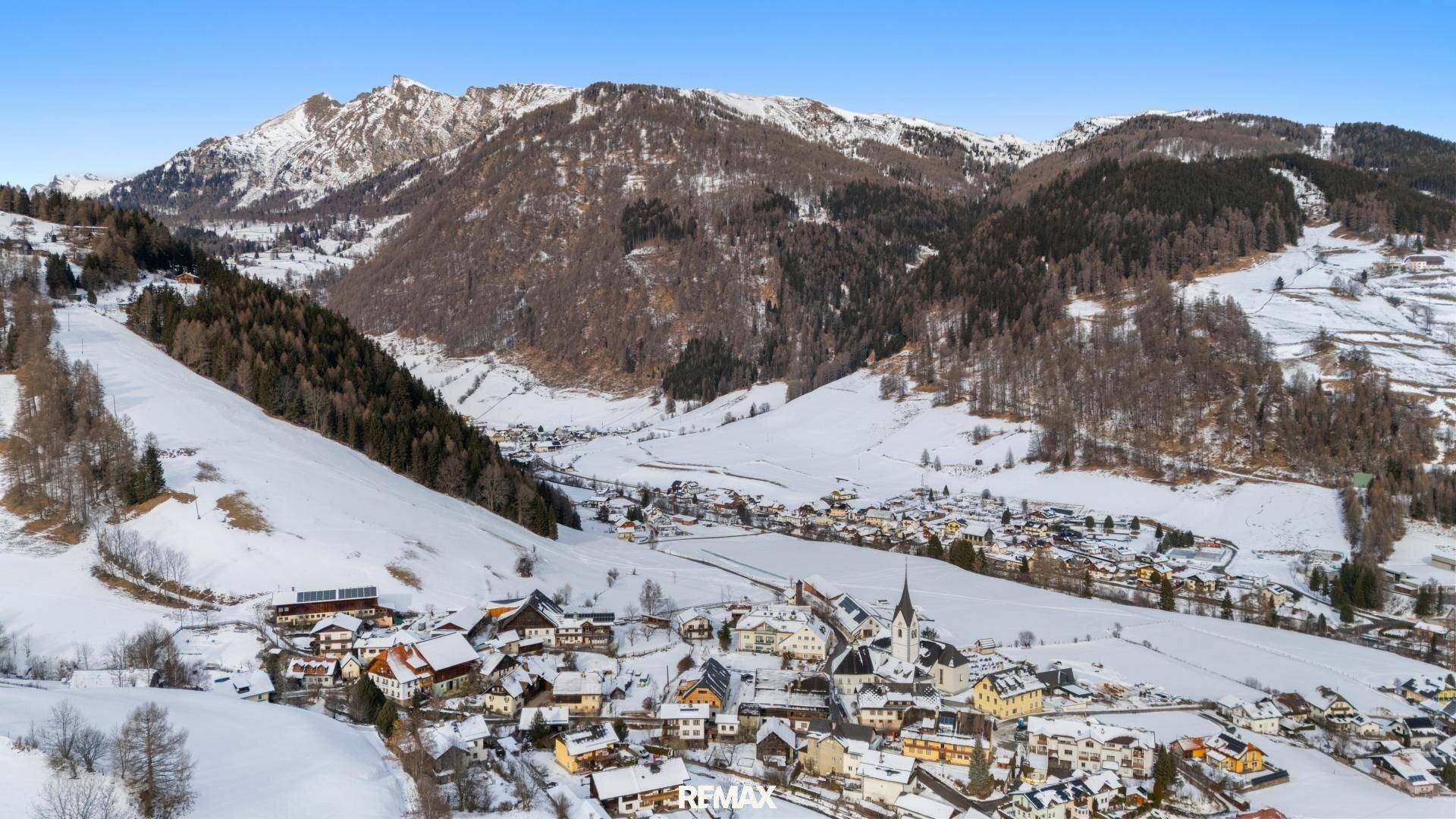 Weitläufiger Blick auf ein schneebedecktes Dorf in einer malerischen Berglandschaft.