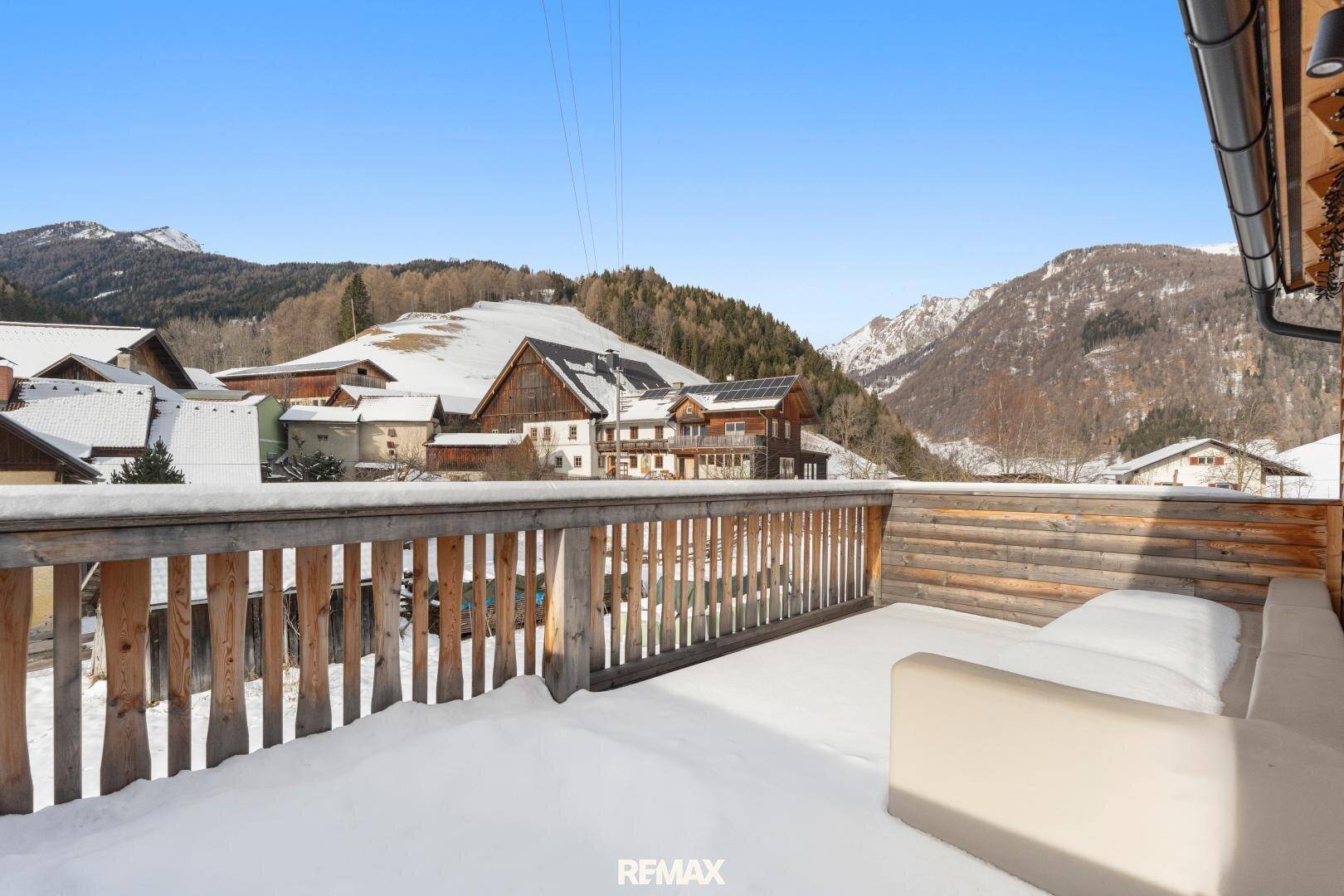 Schneebedeckter Holzbalkon mit Sitzgelegenheiten und weitem Bergblick.