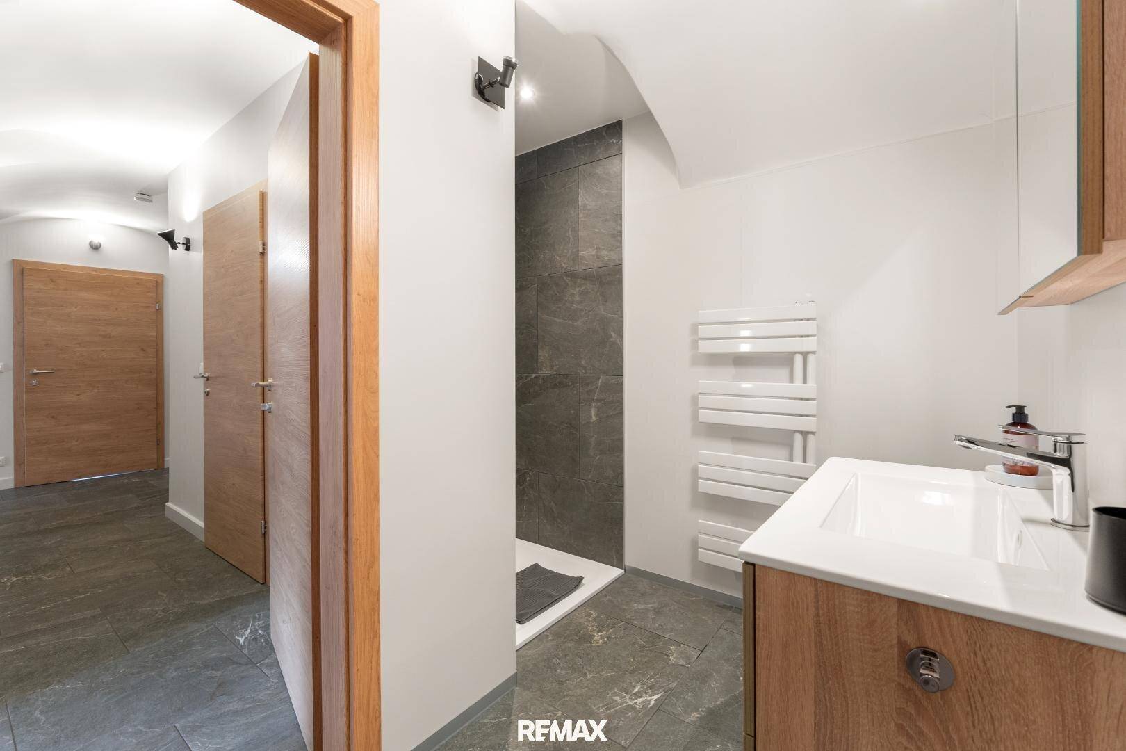 Modernes Badezimmer mit Dusche, beheiztem Handtuchhalter und Holzwaschtisch.
