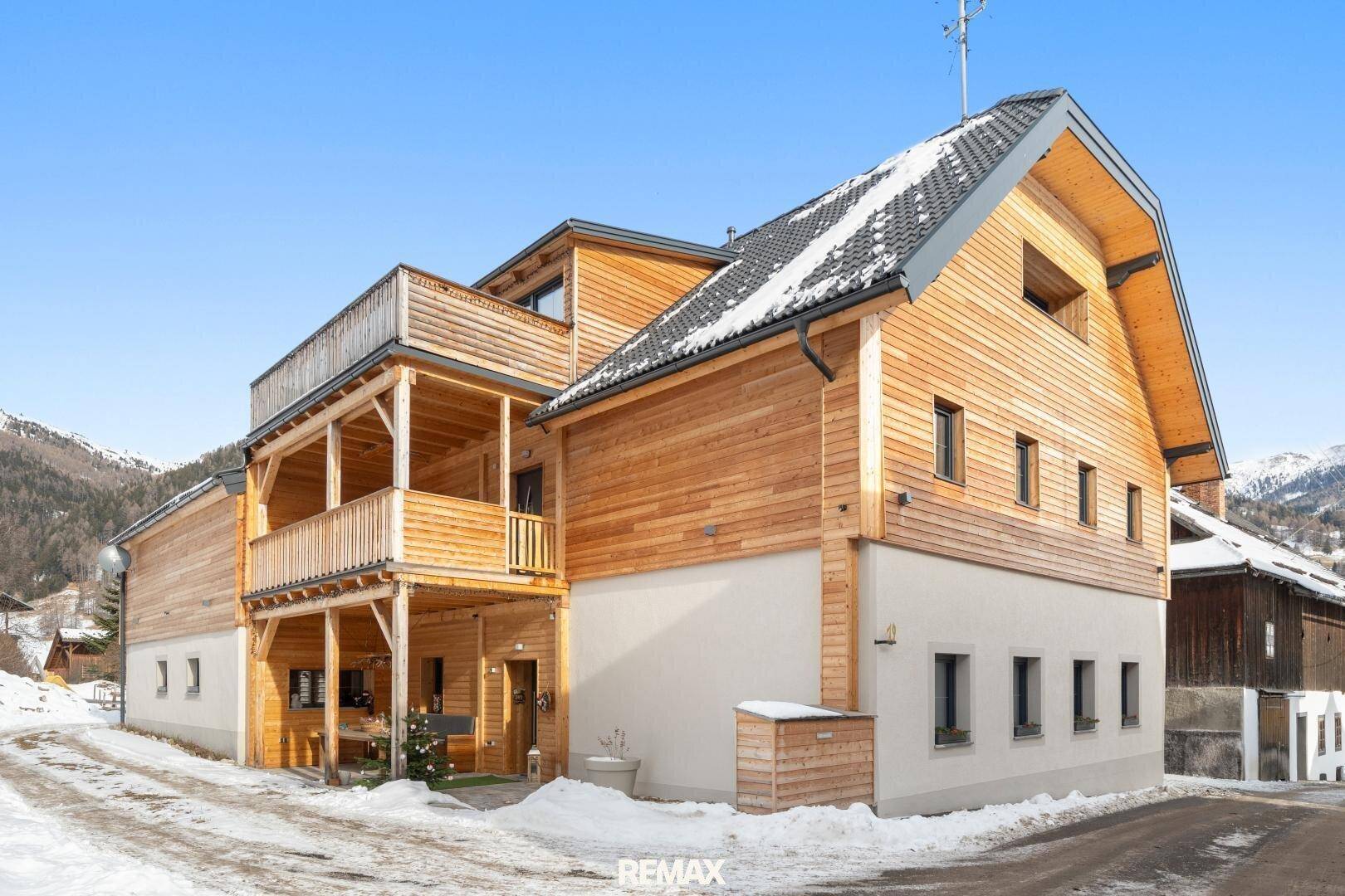 Neubau im alpinen Stil mit Holzfassade und Balkonen, umgeben von Schnee.