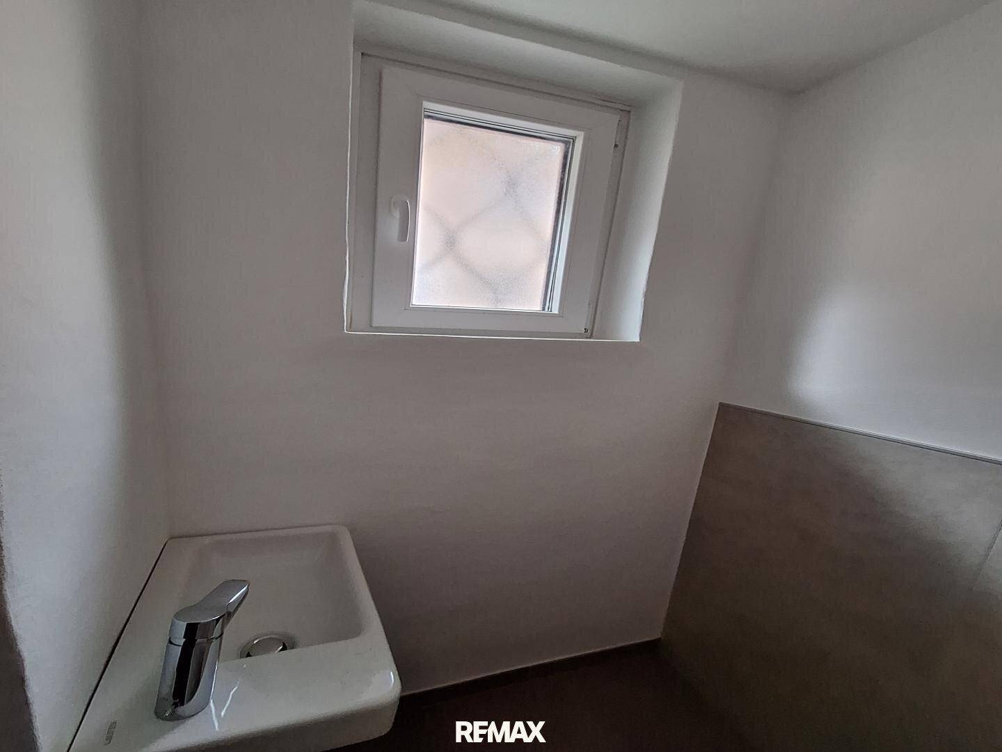 Kleines Gäste-WC mit Waschbecken und Fenster, einfach und funktional gestaltet.