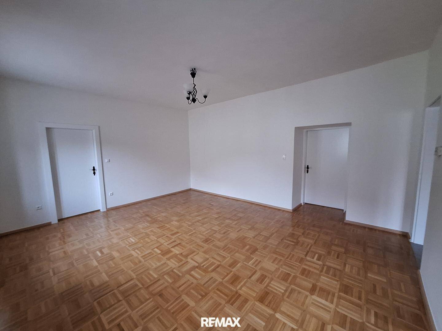 Helles, leeres Wohnzimmer mit klassischem Parkettboden und zwei weißen Türen.