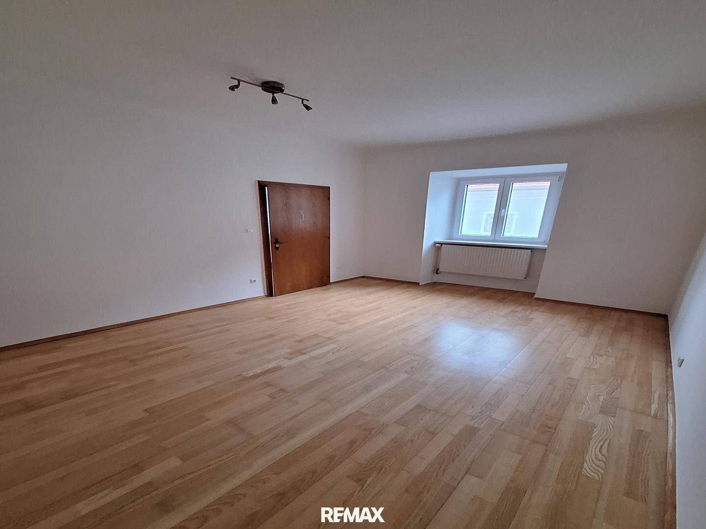 Helles Schlafzimmer mit Holzdielenboden, einer Holztür und einem Fenster mit Heizkörper.