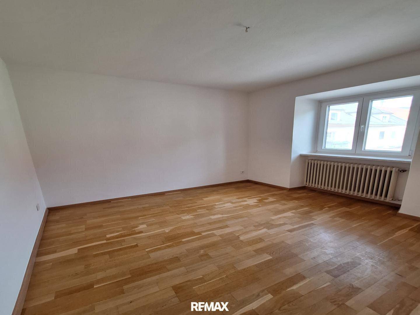 Geräumiges Zimmer mit Parkettboden, weißen Wänden und einem großen Fenster, das viel Licht hereinlässt.