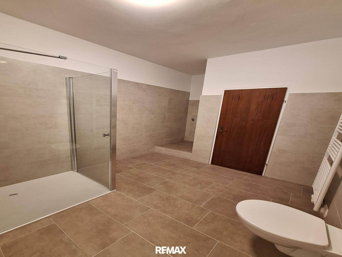 Geräumiges Badezimmer mit Duschkabine, WC, beheiztem Handtuchhalter und einer Holztür.