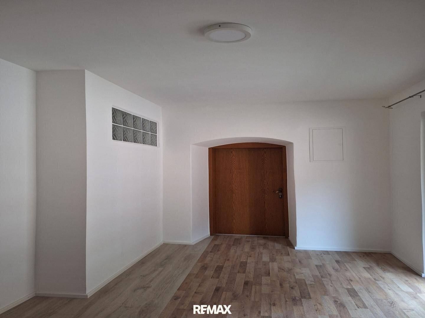 Vielseitiger Raum mit gemischtem Bodenbelag aus Fliesen und Holzdielen sowie einer Holztür.