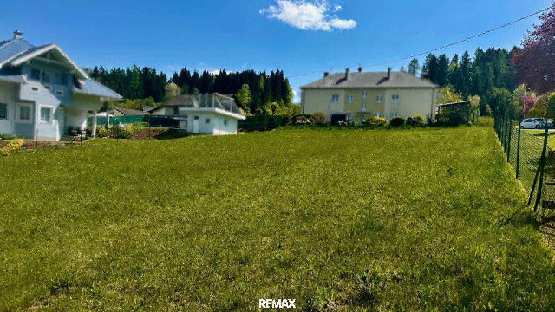 Großes grünes Grundstück mit angrenzenden Wohnhäusern und einem Zaun unter sonnigem Himmel.