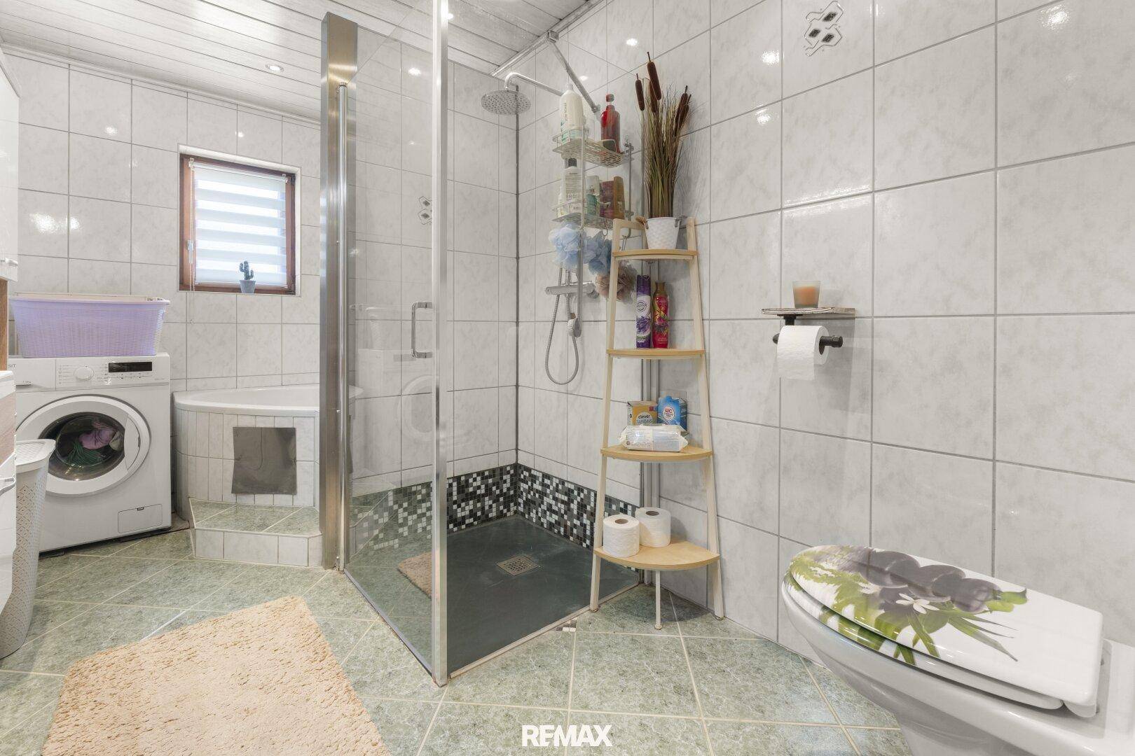Gefliestes Badezimmer mit Dusche, WC, Waschmaschine und kleiner Badewanne.