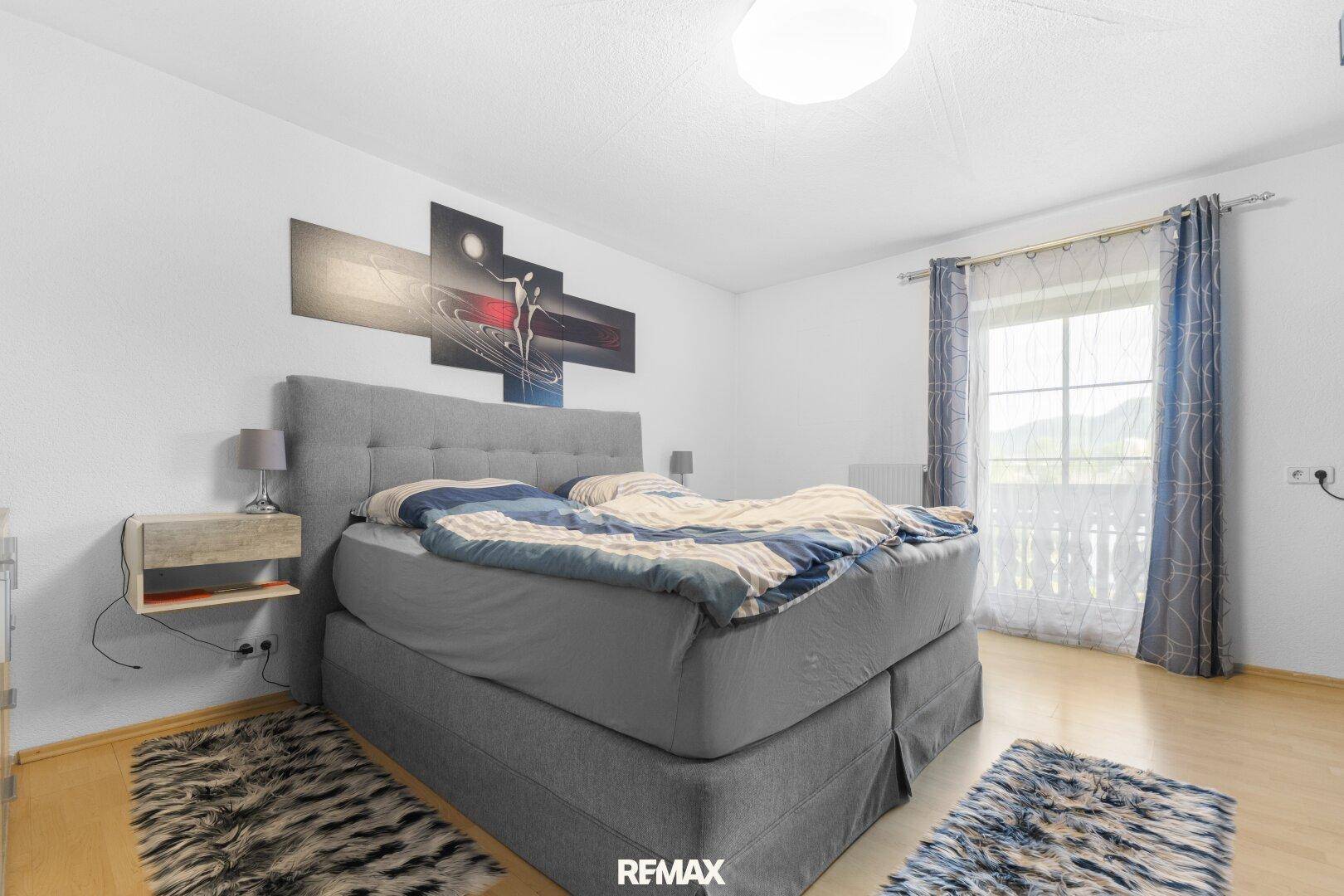 Helles Schlafzimmer mit Doppelbett, Holzboden und Zugang zu einem Balkon.