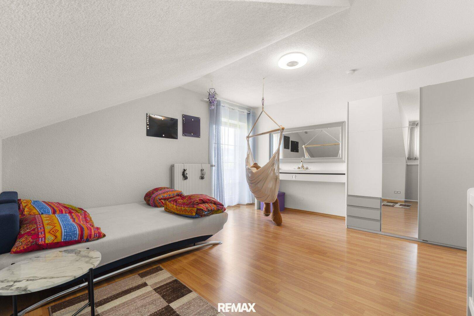 Helles Schlafzimmer mit Dachschrägen, Holzboden und Schreibtischbereich.