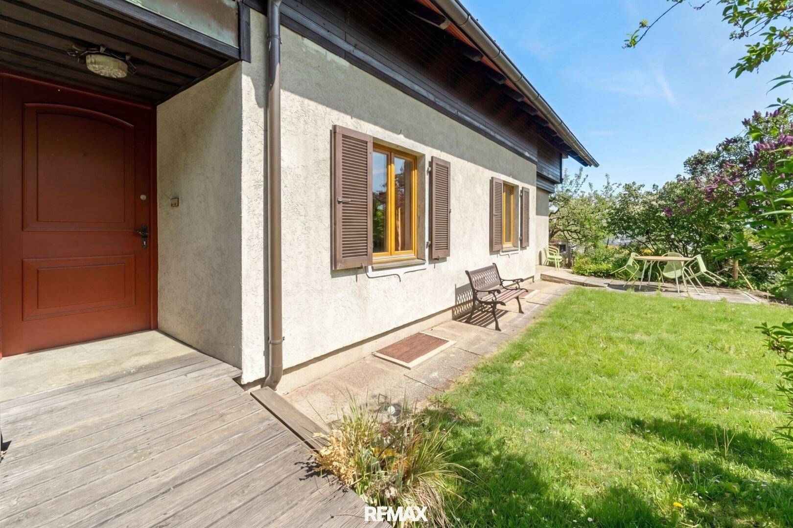 Eingangsbereich des Hauses mit Holztür, Holzterrasse und angrenzendem grünen Garten.