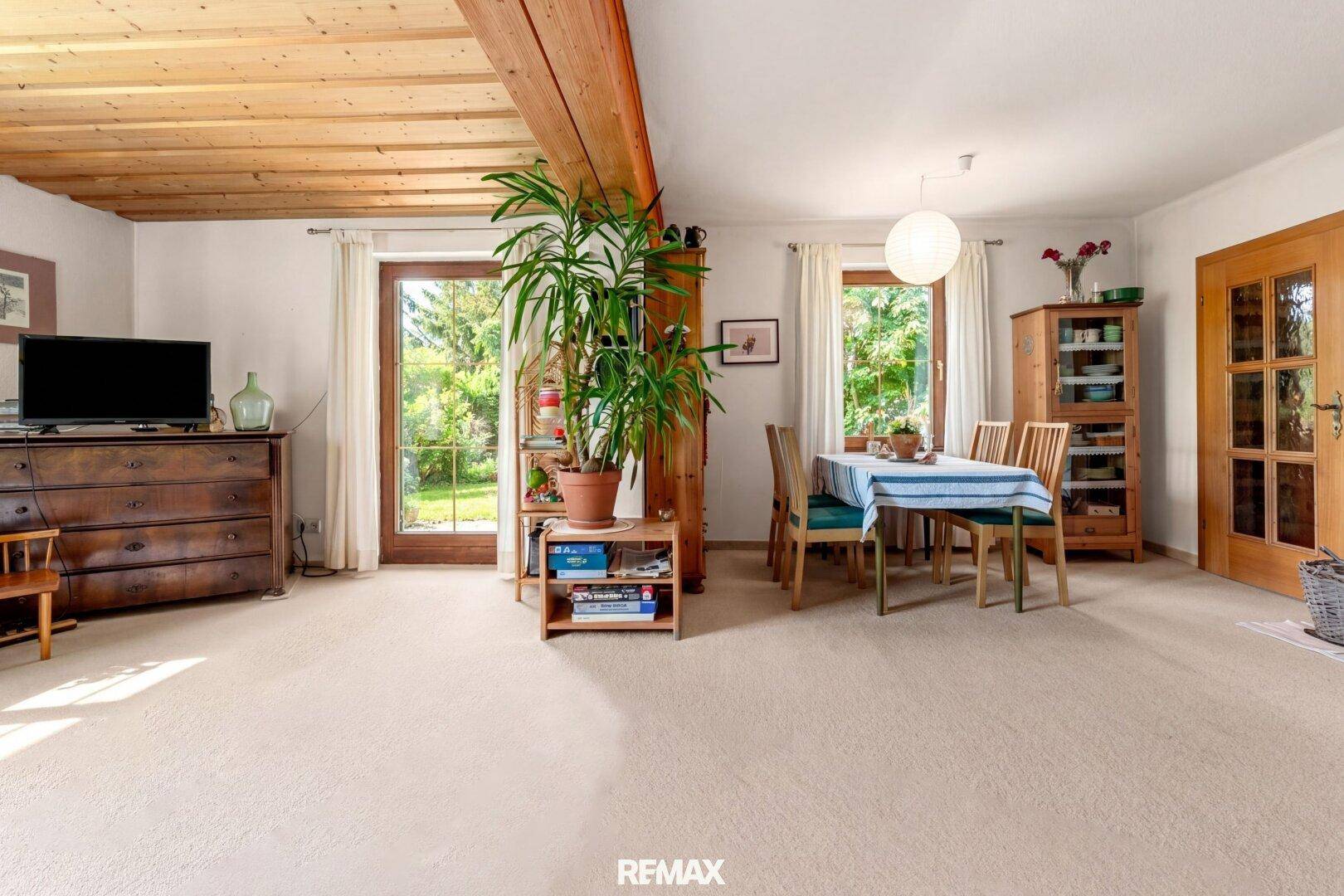 Heller Wohn- und Essbereich mit Teppichboden, Holzbalkendecke und Zugang zum Garten.