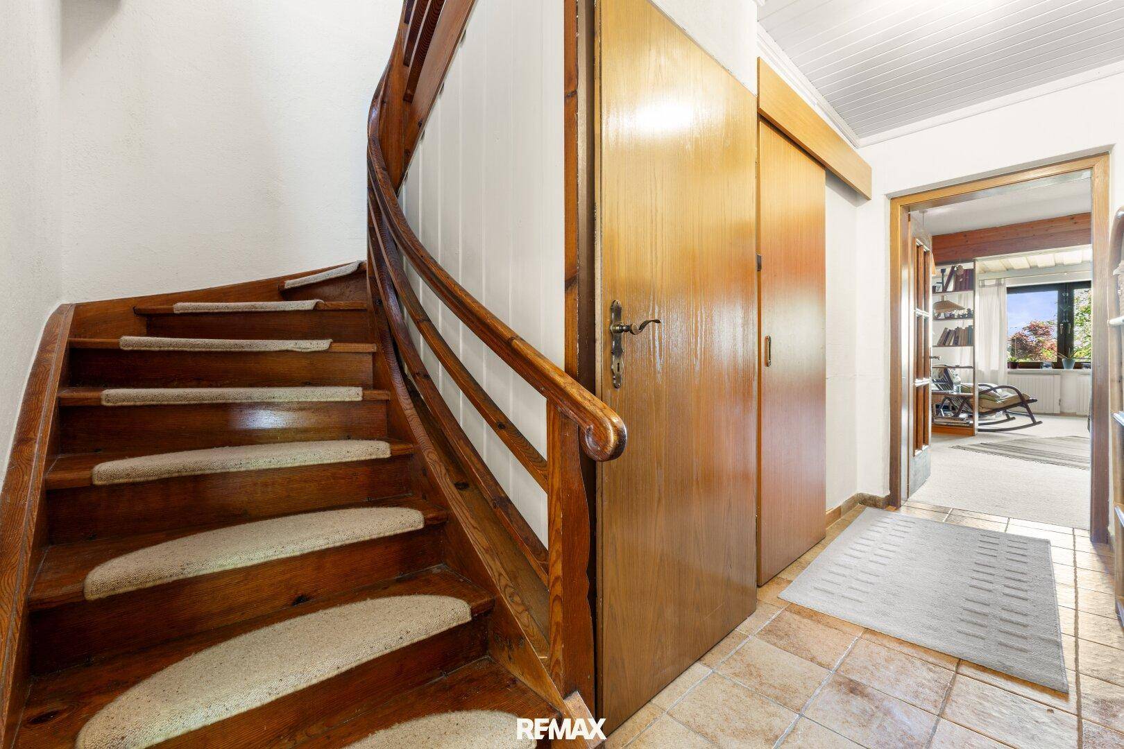 Helle Diele mit rustikaler Holztreppe und Fliesenboden, die zu weiteren Räumen führt.