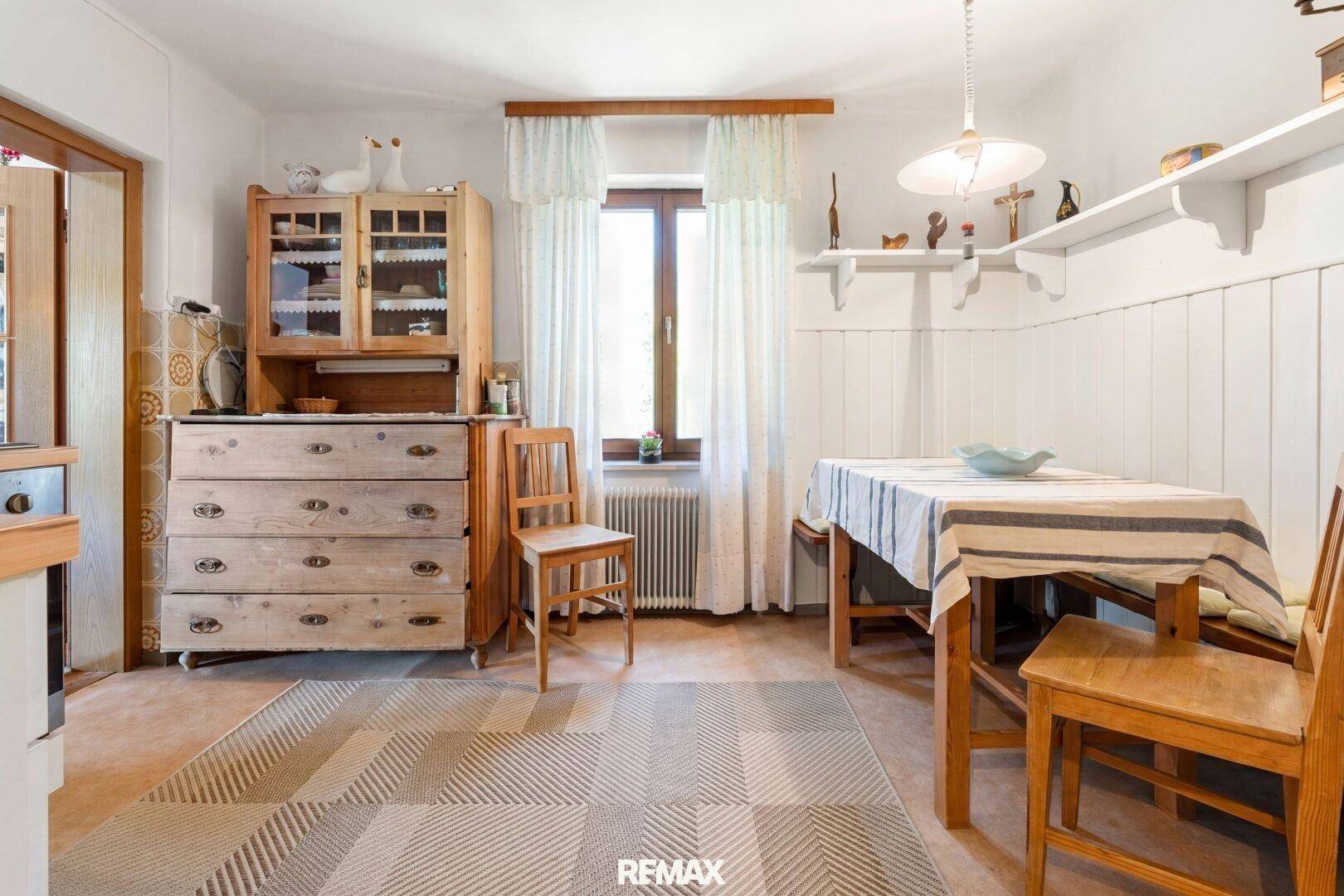 Gemütliche Wohnküche mit traditionellen Holzmöbeln, Esstisch und Fenster mit Vorhängen.
