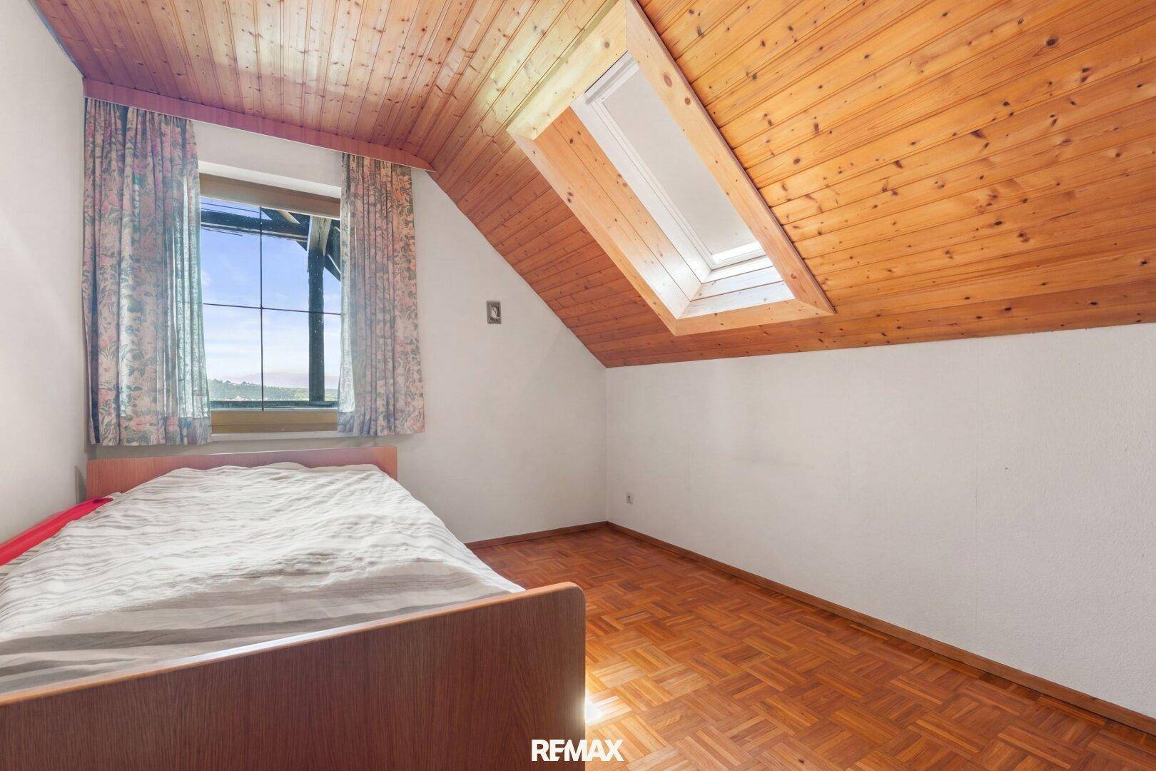 Helles Schlafzimmer mit Parkettboden, Dachschräge und Dachfenster für natürliches Licht.