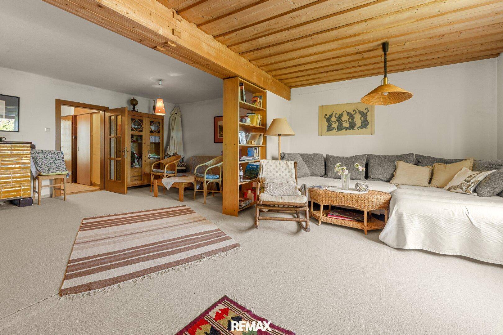 Geräumiges Wohnzimmer mit Teppichboden, Holzbalkendecke und gemütlicher Sitzecke.