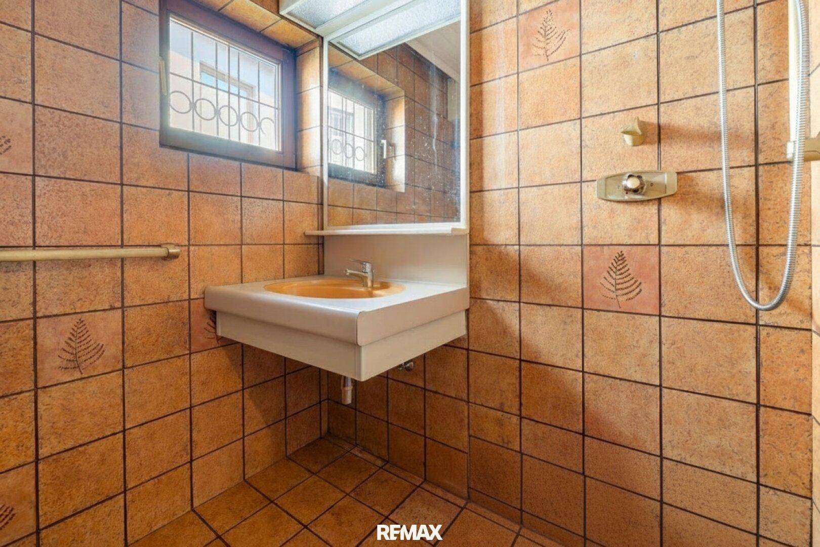 Badezimmer mit orangefarbenem Waschbecken, braunen Fliesen und Duschbereich.