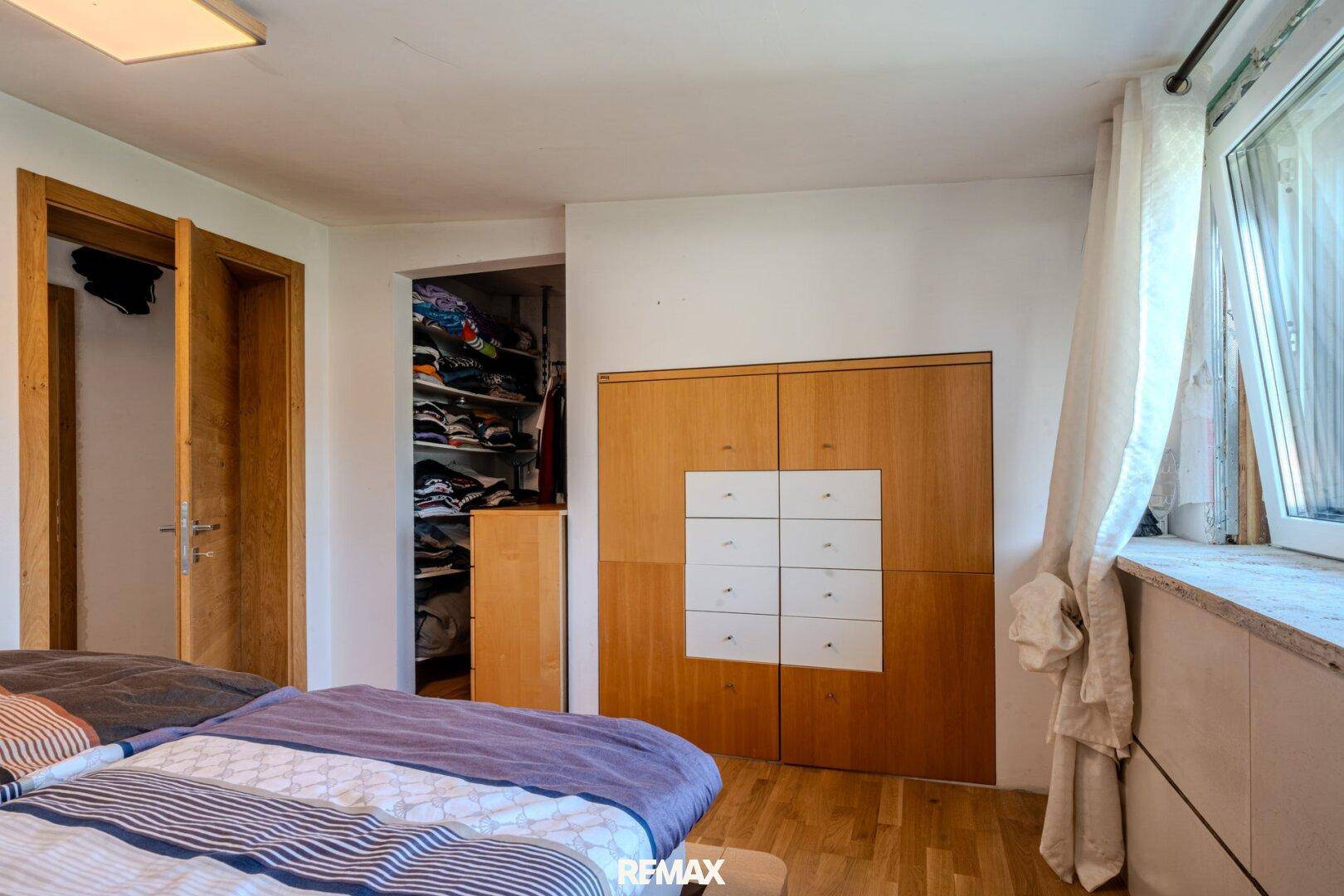 Schlafzimmer mit Holzboden, Einbauschränken und Zugang zu einem begehbaren Kleiderschrank.