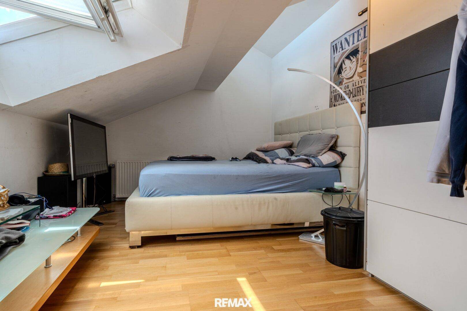 Schlafzimmer im Dachgeschoss mit Dachfenster, Holzboden und modernem Bett.