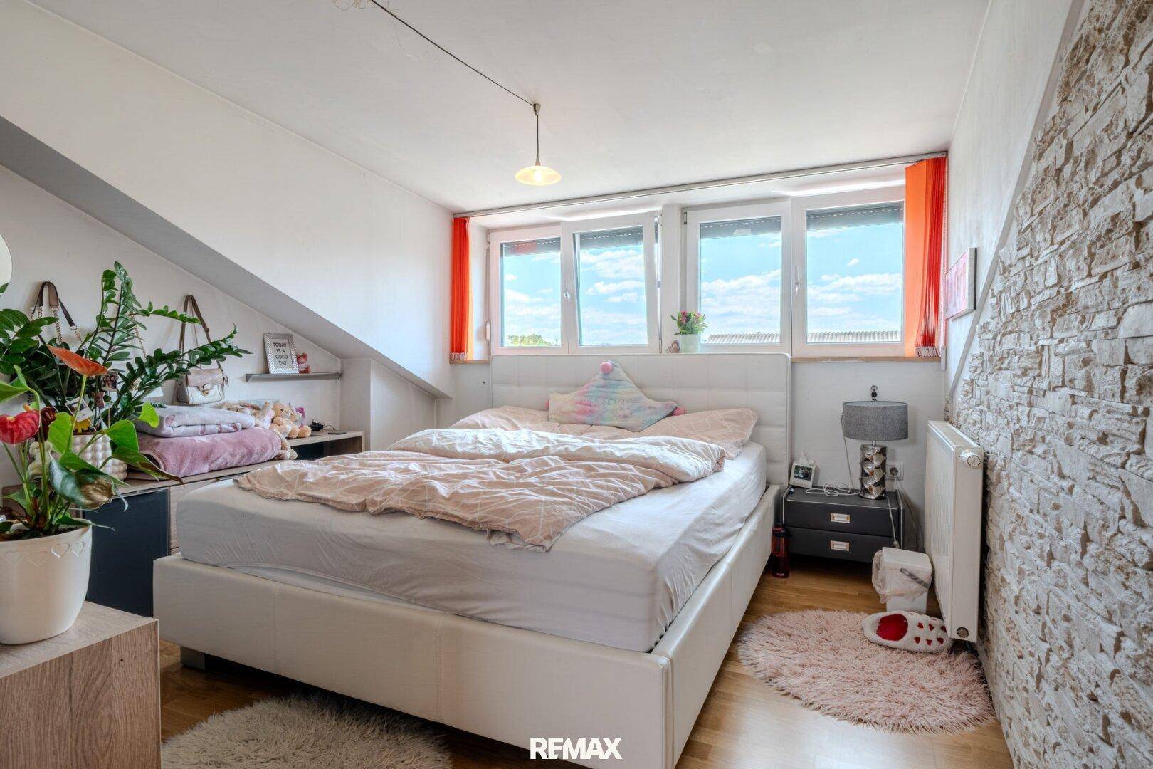 Gemütliches Schlafzimmer mit Holzboden, Ziegelwand und farbigen Vorhängen.