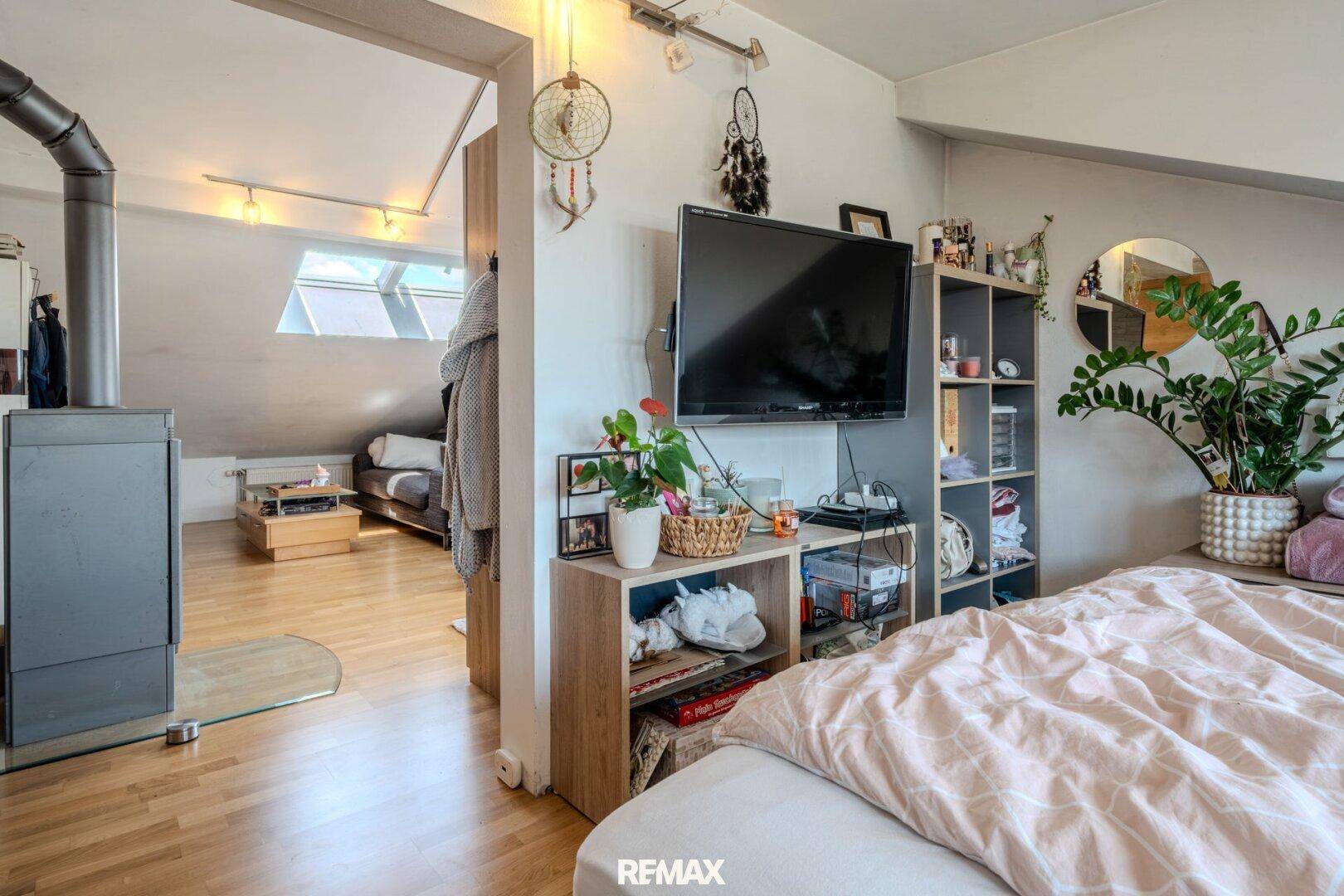 Schlafzimmer mit Holzboden, Fernseher und Blick in einen weiteren Wohnbereich.