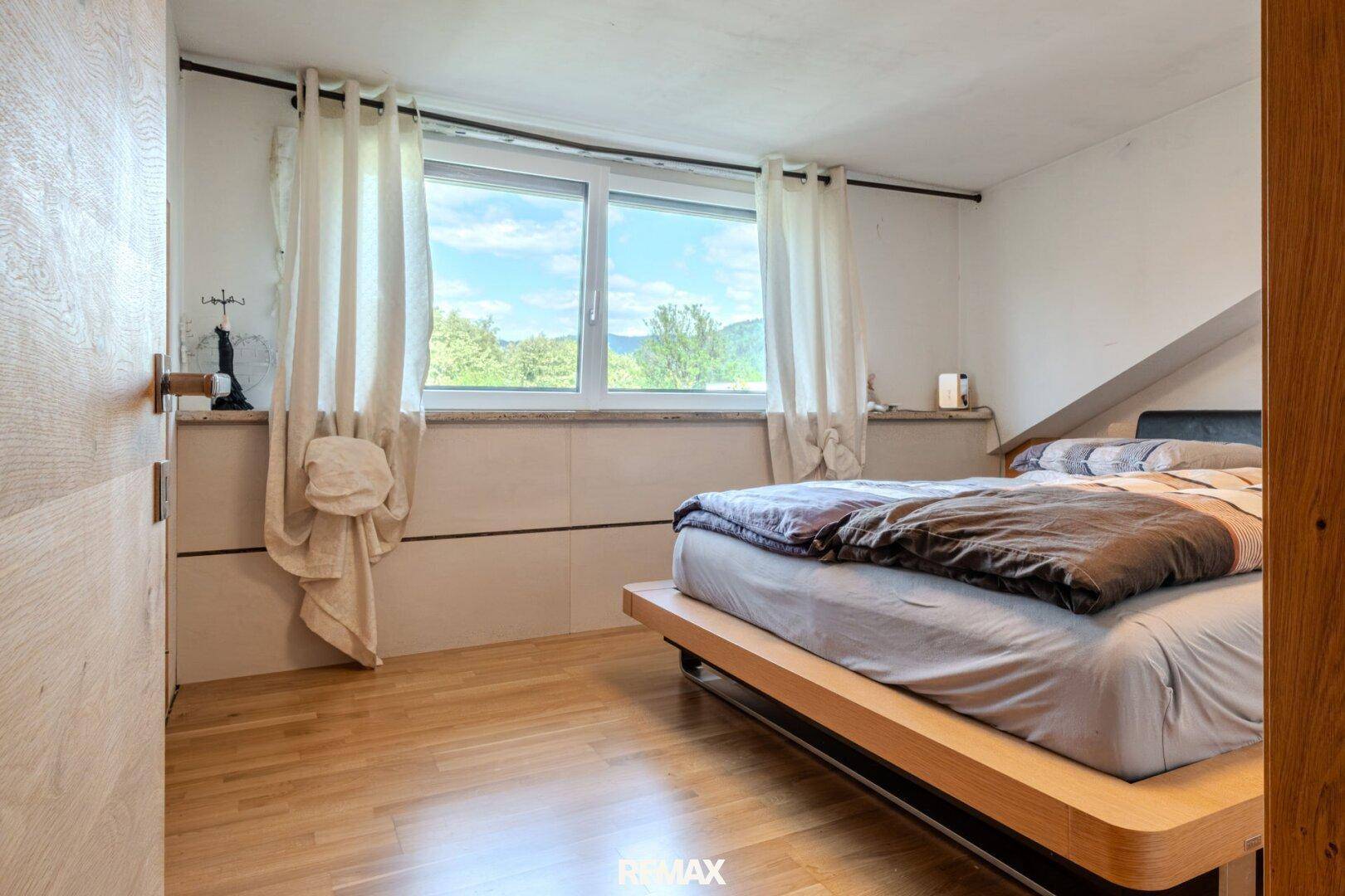Schlafzimmer mit Holzboden, großem Fenster und hellem Tageslicht.