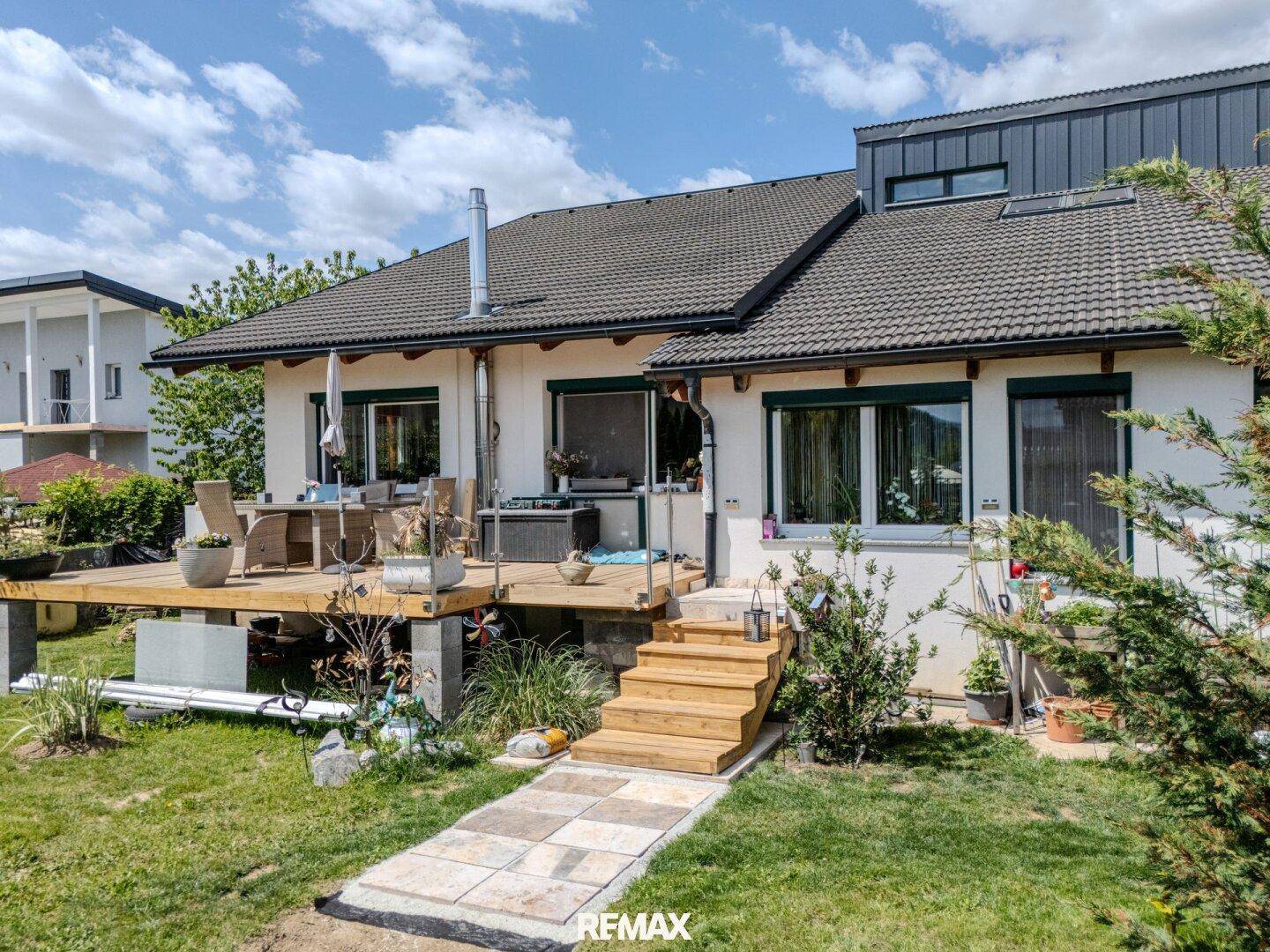 Holzterrasse mit Treppe zum Garten, umgeben von Grünflächen und Bäumen.