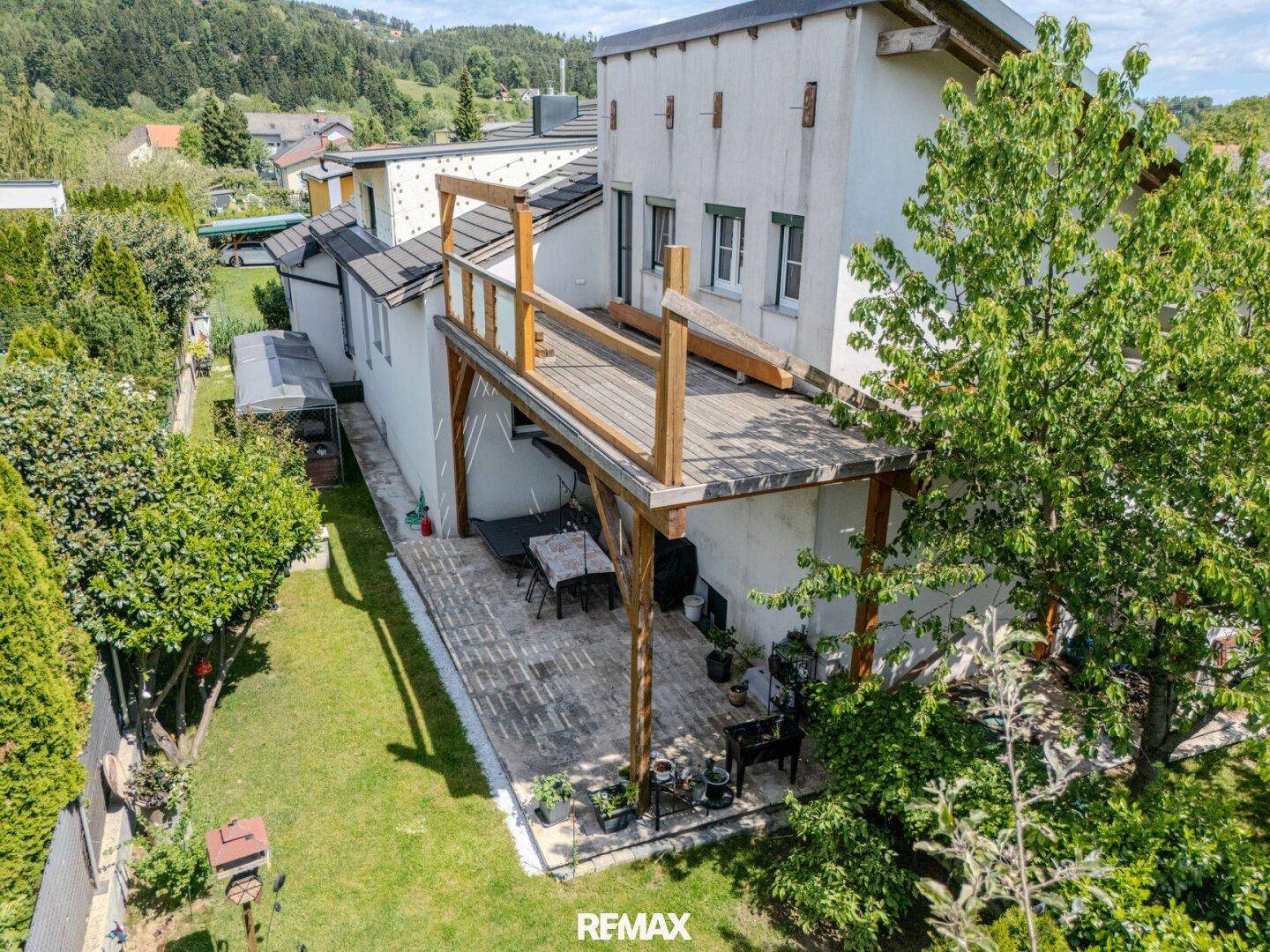 Hinterhof mit gepflasterter Terrasse, Rasenfläche und erhöhtem Holzbalkon.