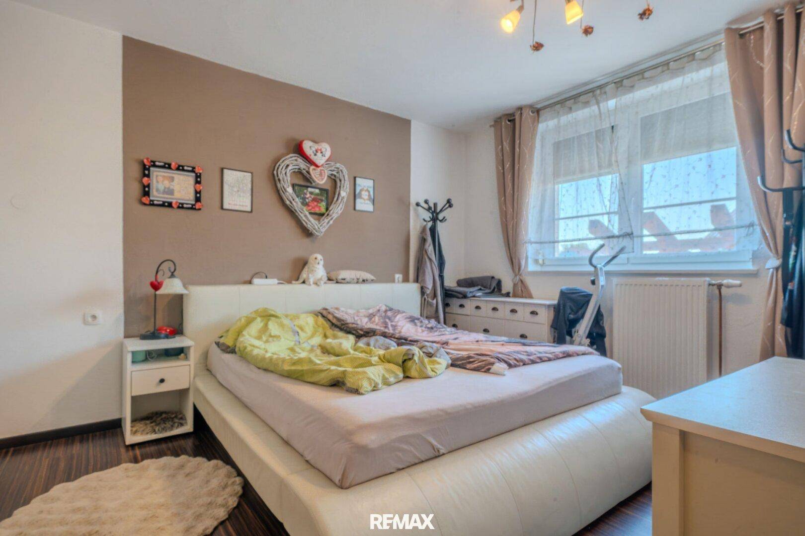 Schlafzimmer mit Holzboden, brauner Akzentwand und großem Fenster.