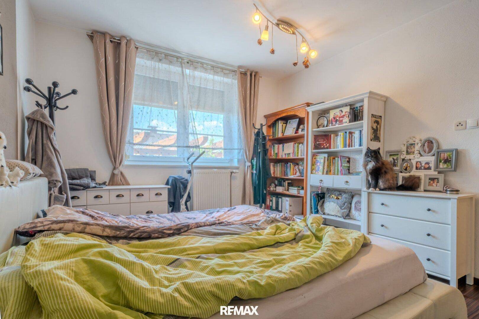Schlafzimmer mit Holzboden, Bücherregal und großem Fenster.