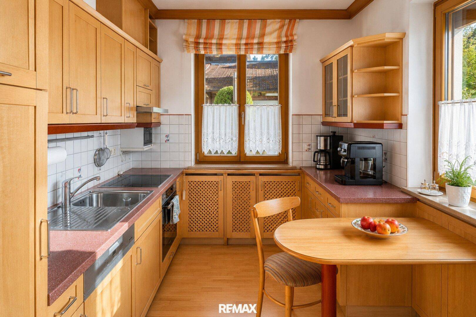 Funktionale Küche mit Holzschränken, Essbereich und Fenster mit Blick nach draußen.