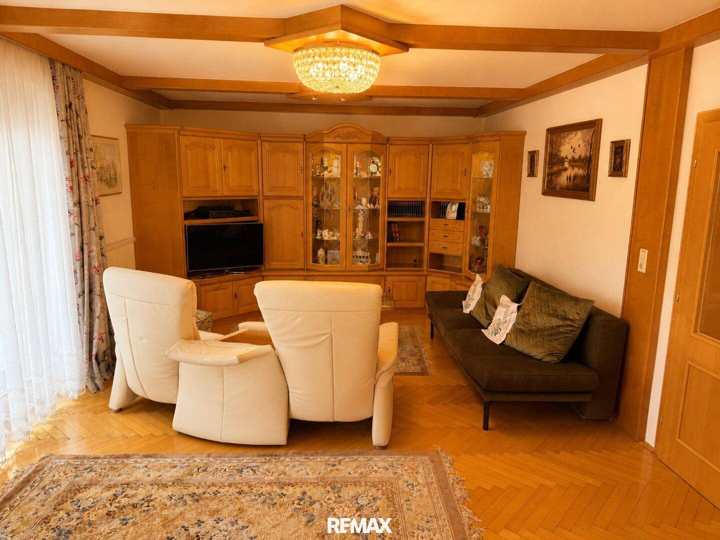 Geräumiges Wohnzimmer mit Holzboden, großer Schrankwand und bequemen Sitzmöbeln.