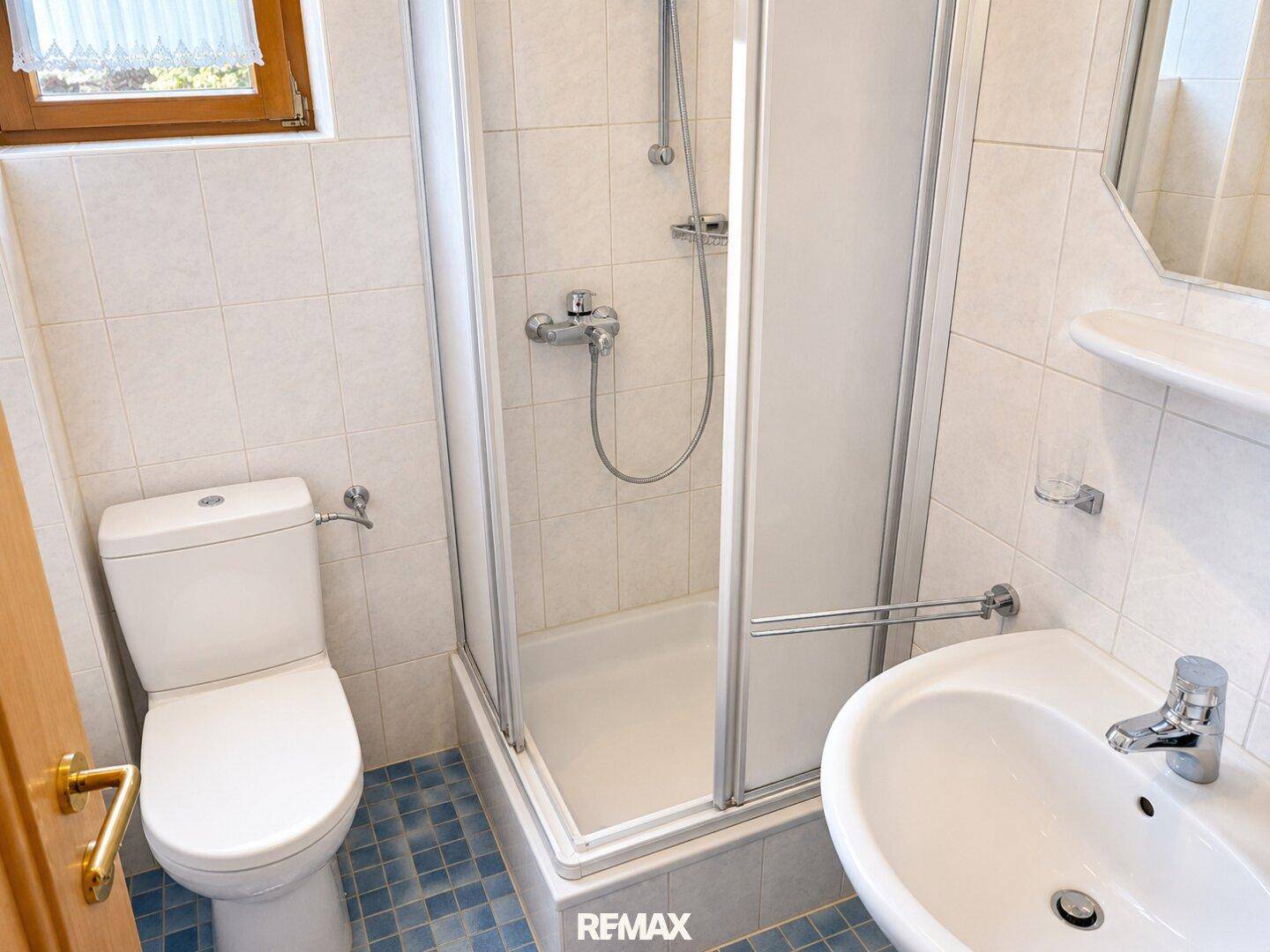 Kleines Badezimmer mit Dusche, WC und Waschbecken, ausgestattet mit blauen Fliesen.