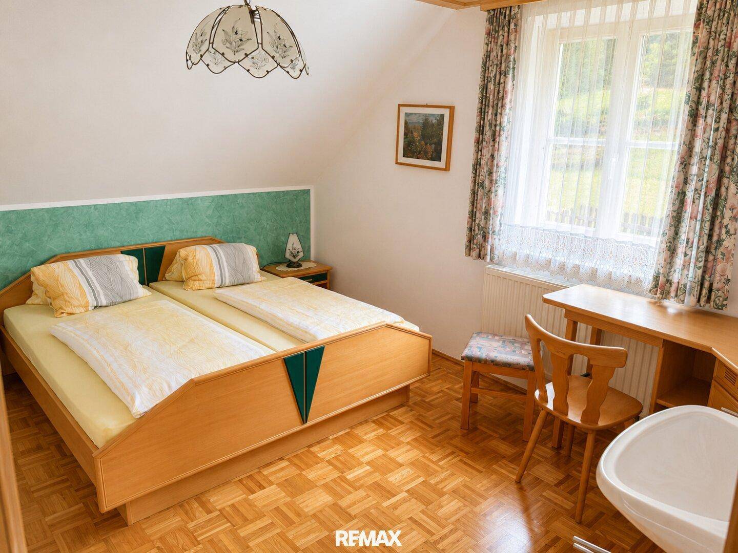 Helles Schlafzimmer mit Holzboden, Doppelbett und Fenster mit Blick ins Grüne.